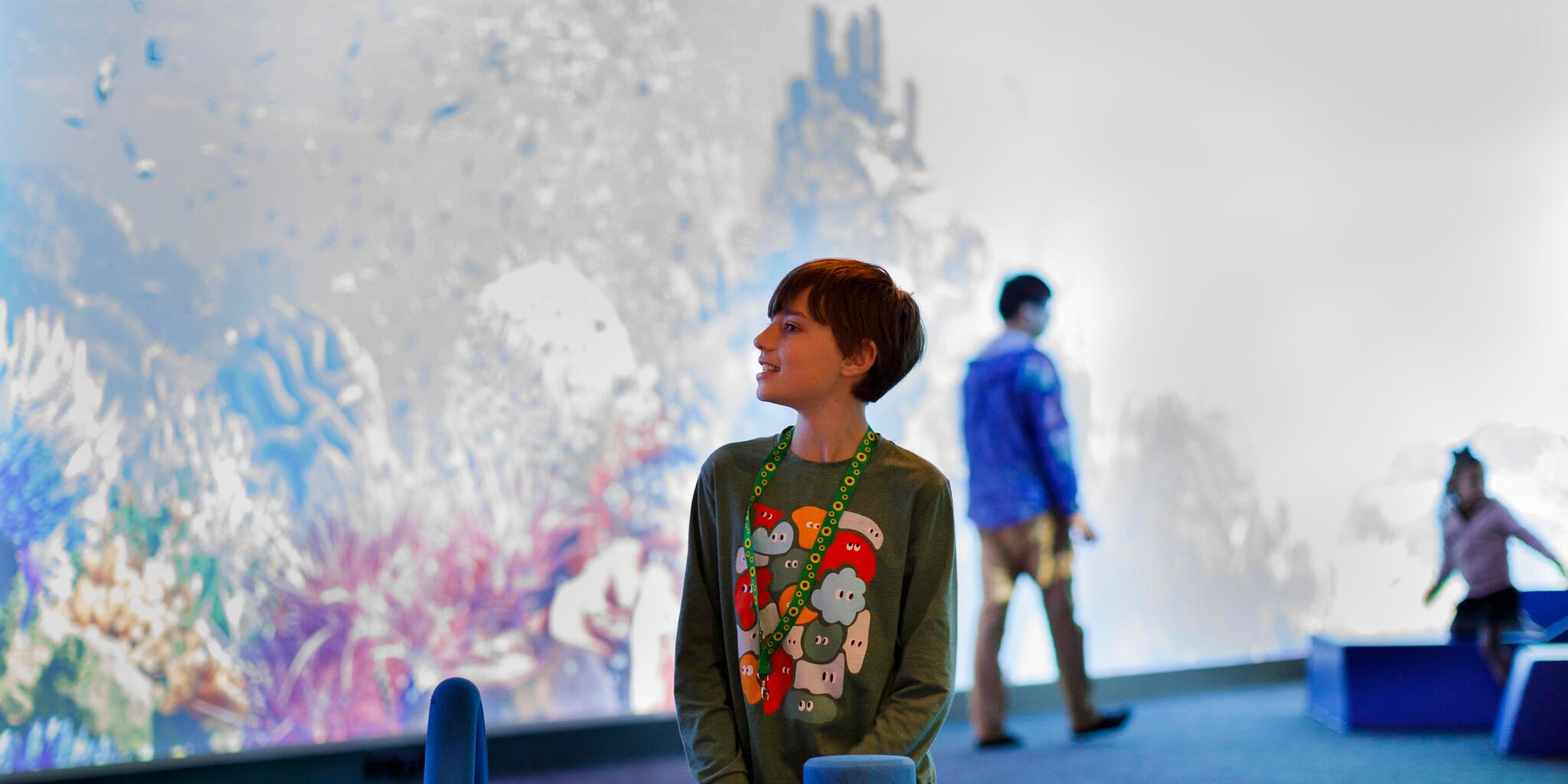 Young boy with short, dark hair, wearing a grey shirt with colourful print and sunflower lanyard playing with large blue blocks.