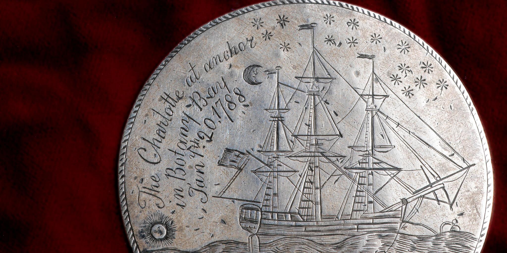 The CHARLOTTE Medal, a silver disc engraved on both sides. This photograph shows engraved a fully-rigged ship, the sun is near the horizon line on the lower left whilst a crescent moon and stars are inscribed on the upper right. Above are inscribed the words 'The CHARLOTTE at anchor / in Botany Bay / Jany. th 20, / 1788'.