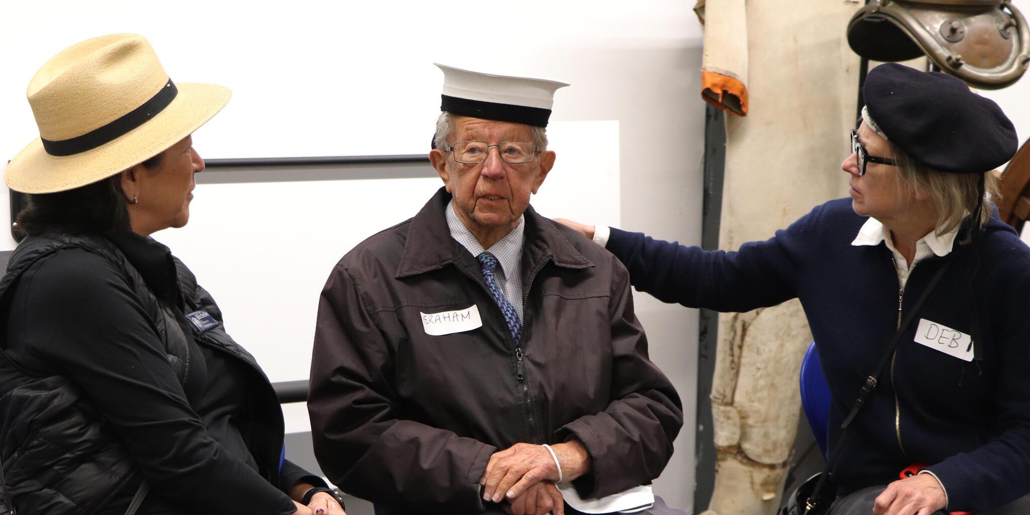 Two ladies sitting either side of an older gentleman wearing a sailors hat.