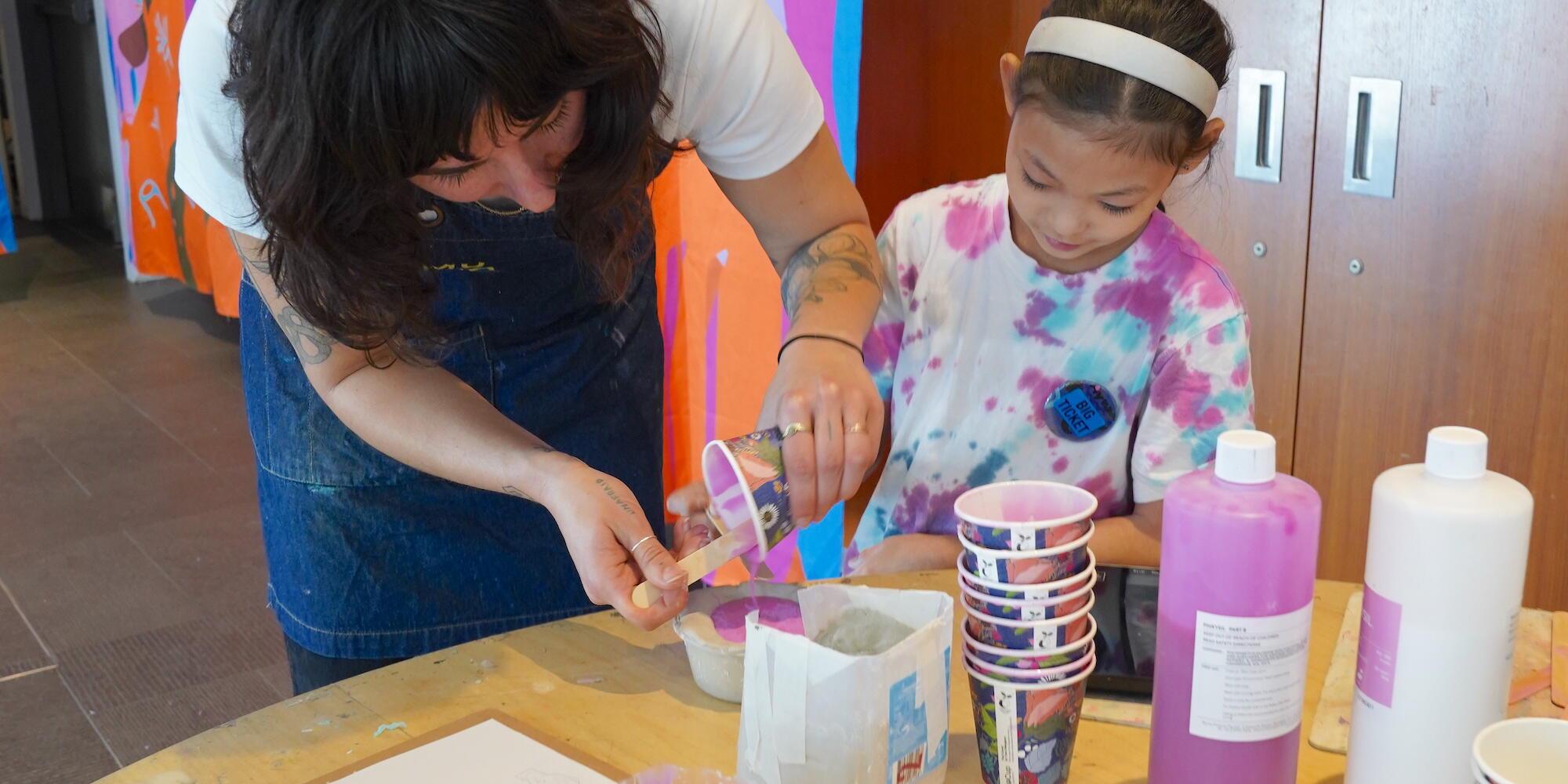 a lady and a girl standing behind a table working together on creating a mould for an artwok.