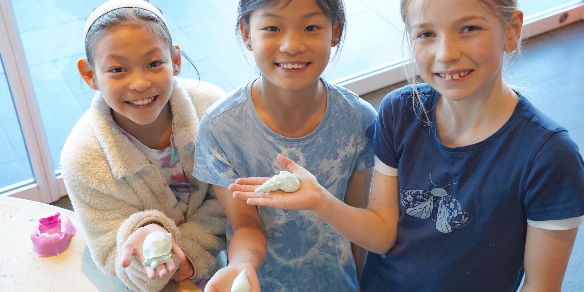 3 girls holding their artworks which look like shells 