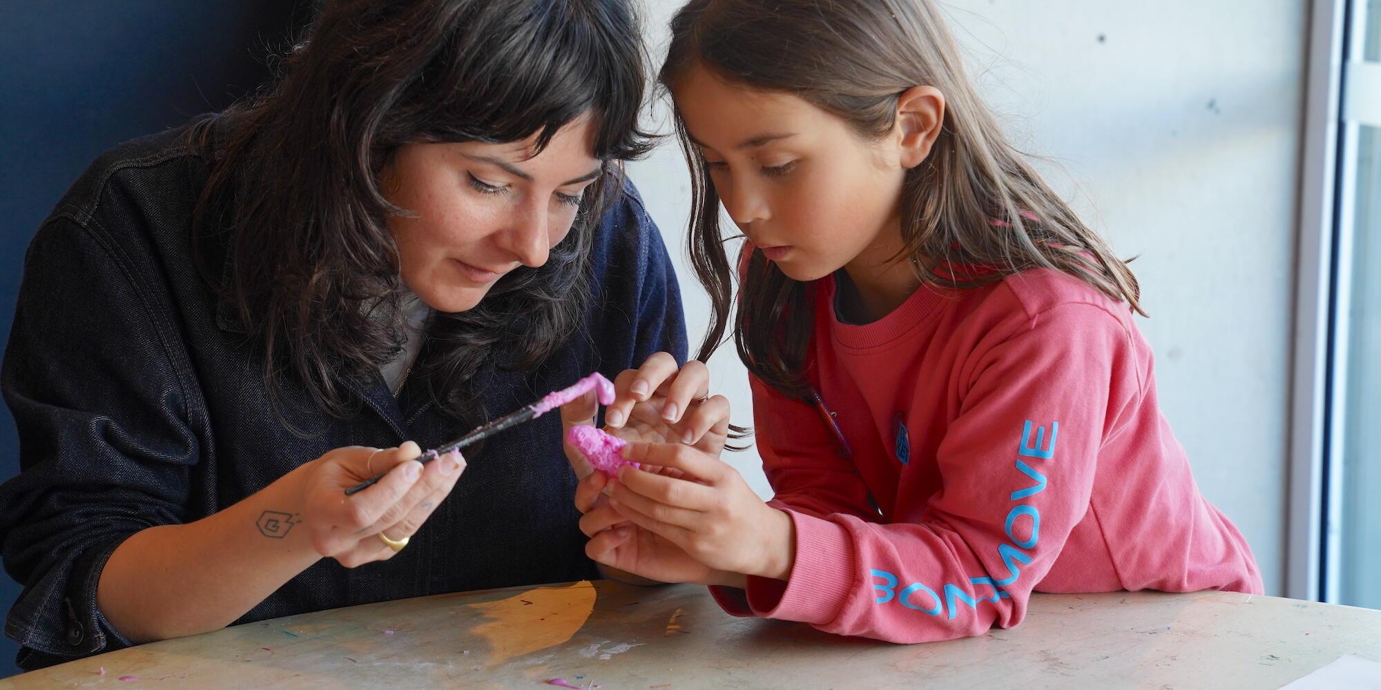 A girl in a red top with an adult woman wearing black, working together on a craft activity.