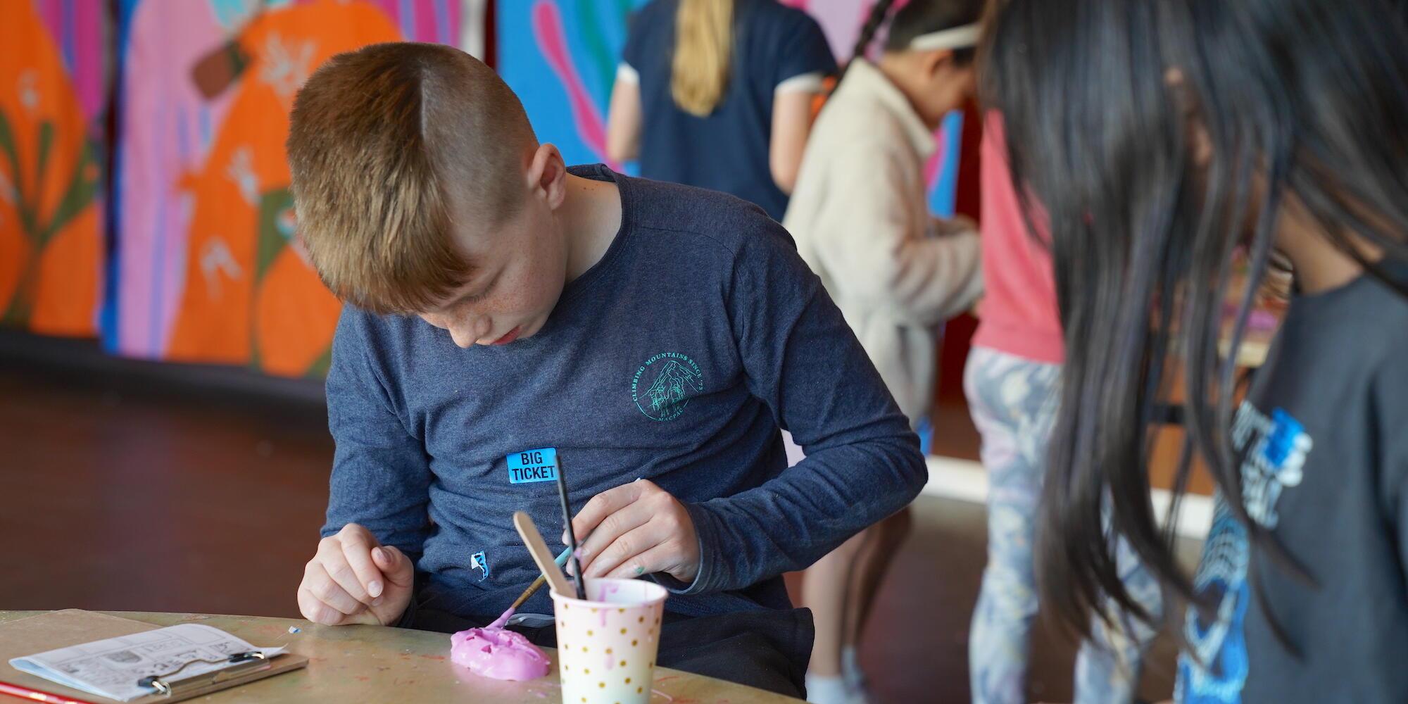 A boy wearing a dark blue top looking down at the mould he is making. 