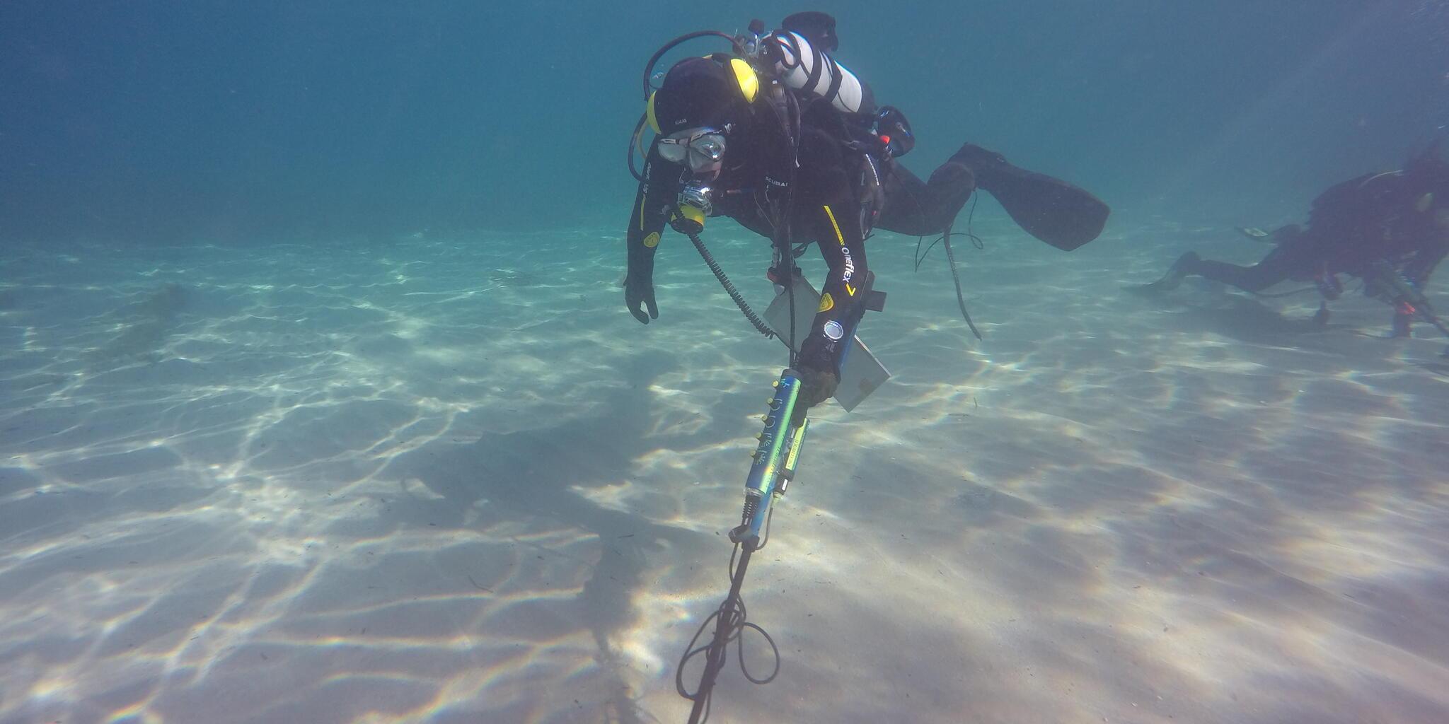 Underwater phptpgraph of a diver holding a metal detector