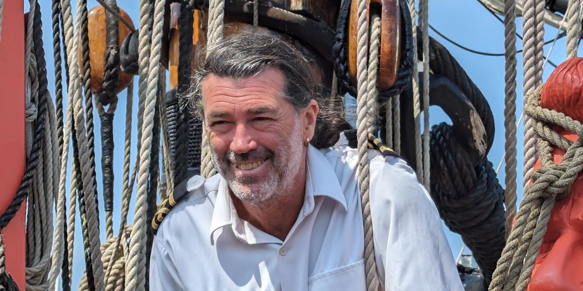 photo of captain of endeavour standing and smiling, with the mast and ropes behind him. 