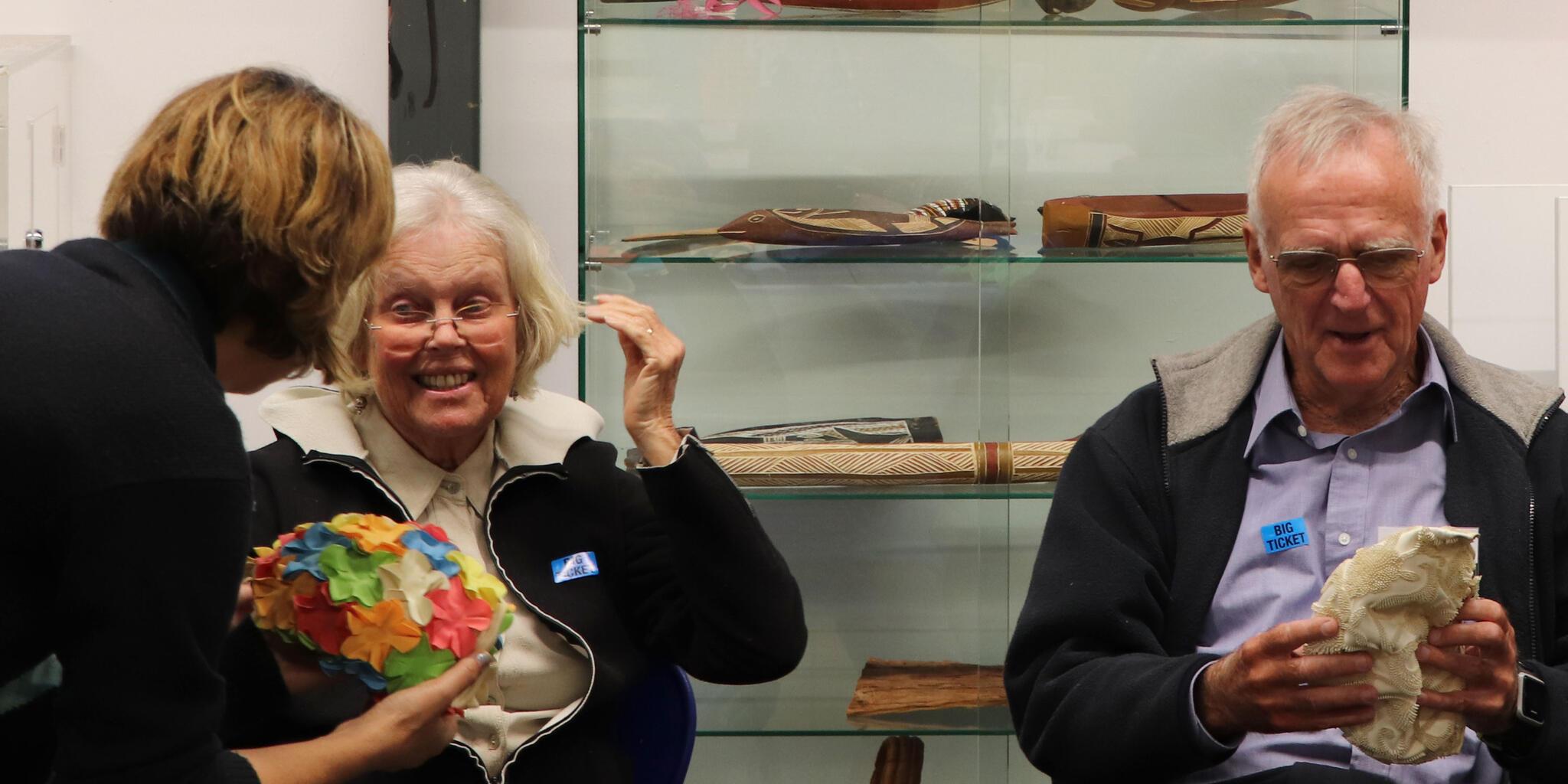 Photo of two older people, a man and woman, looking at bathing caps, talking to a museum staf member. 