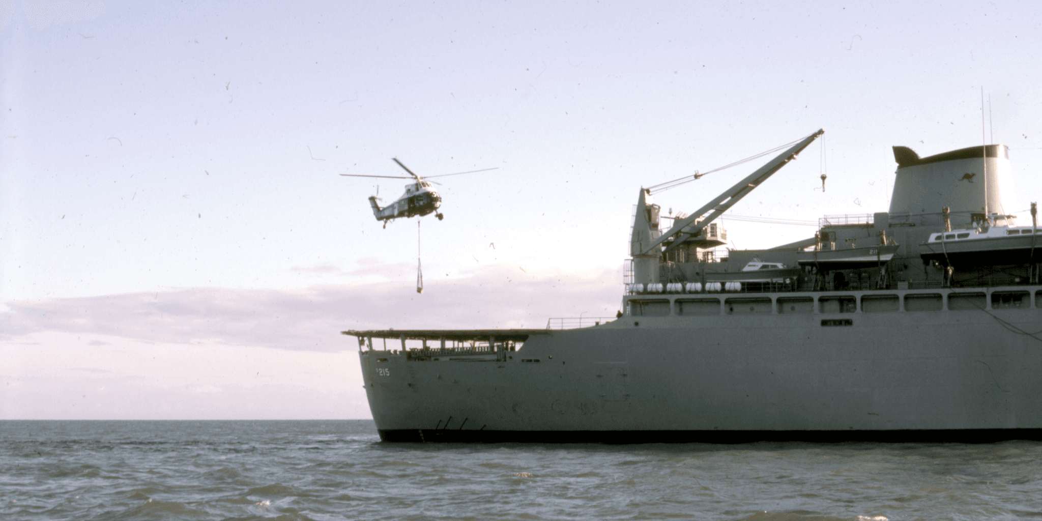 A naval ship in the distance, with a helicopter approaching. 