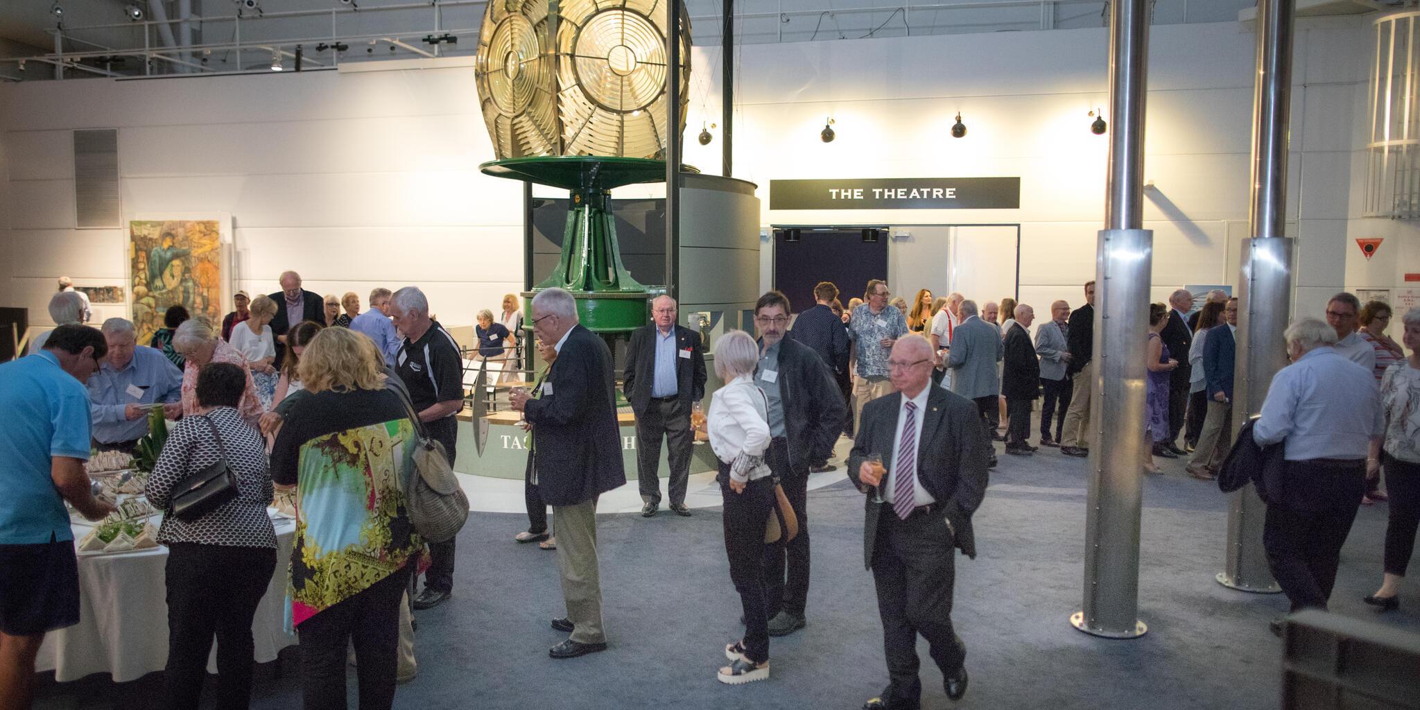 photo of a crowd of people standing around a historical lighthouse lens. 