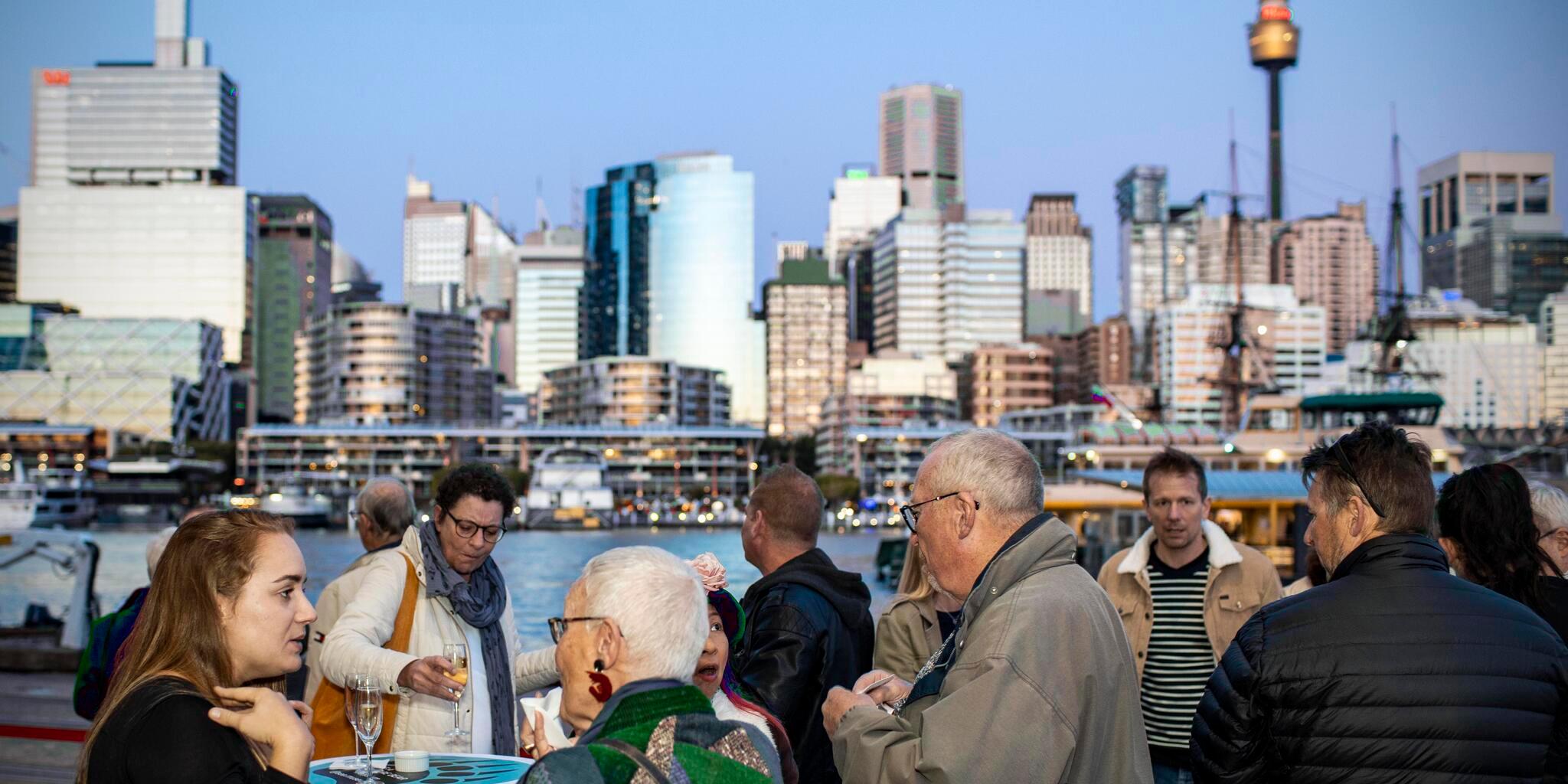 Guests standing outside on the museum boardwalk, enjoying canapés outdoors at the opening with city views.