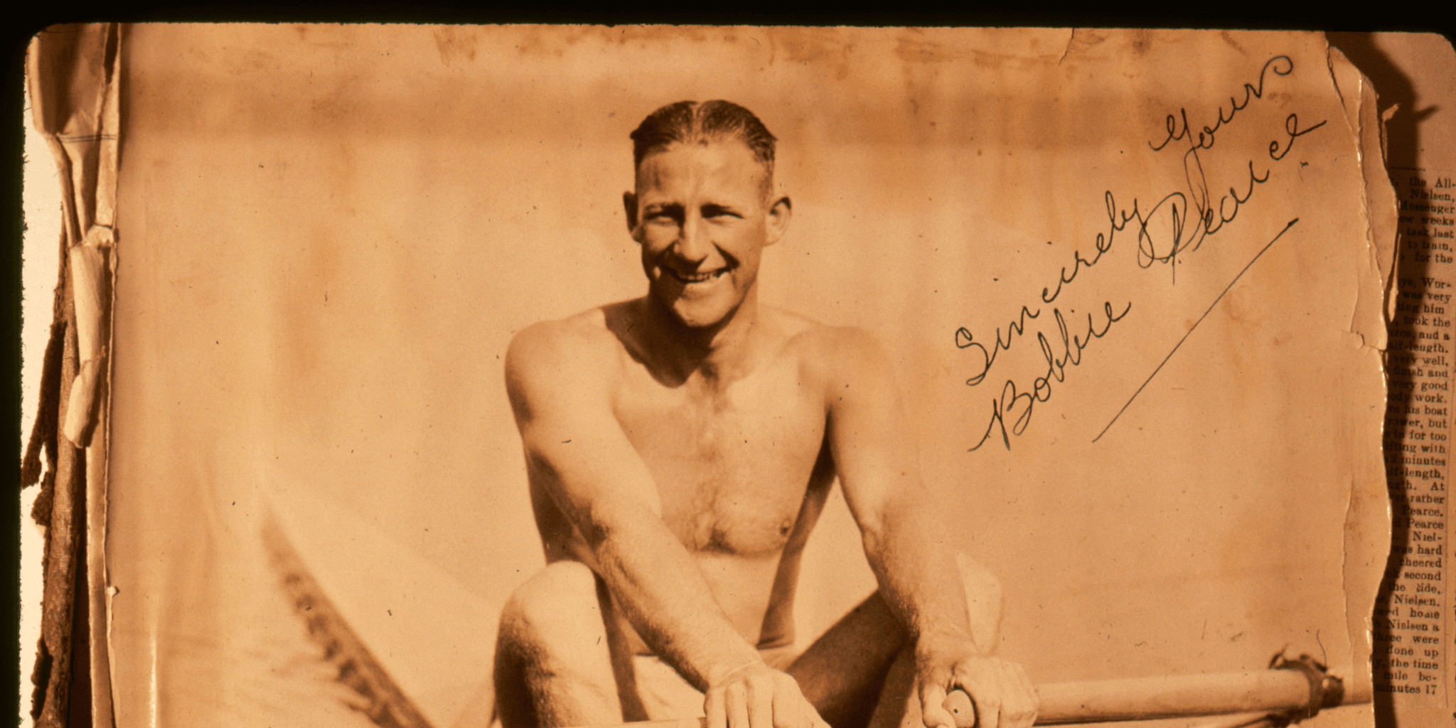 Black and White photo on very yellowed paper of a shirtless man with short hair in a row boat. 