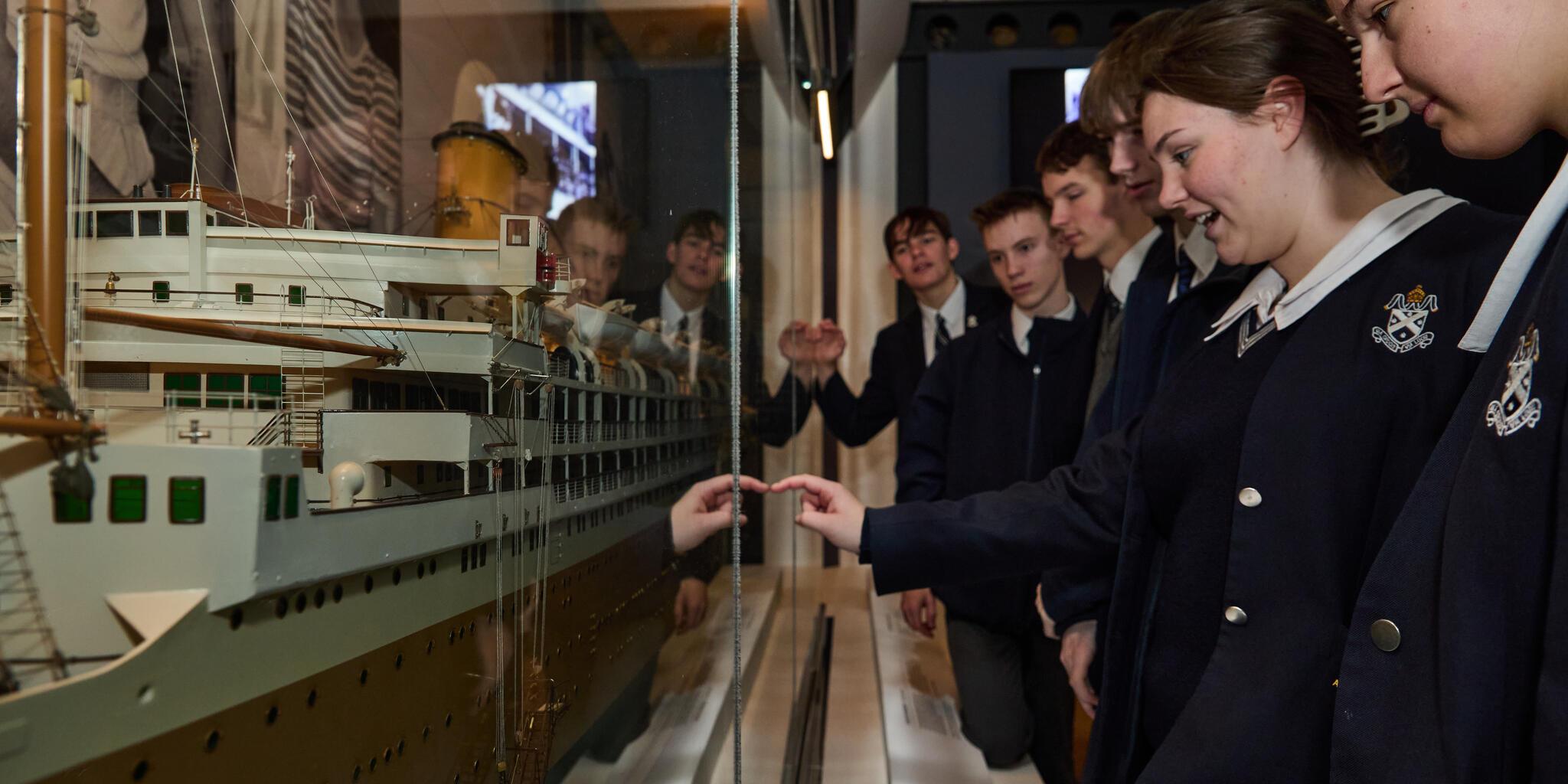 image of a model of an ocean liner in a display case, with a line of high school students looking at it. 