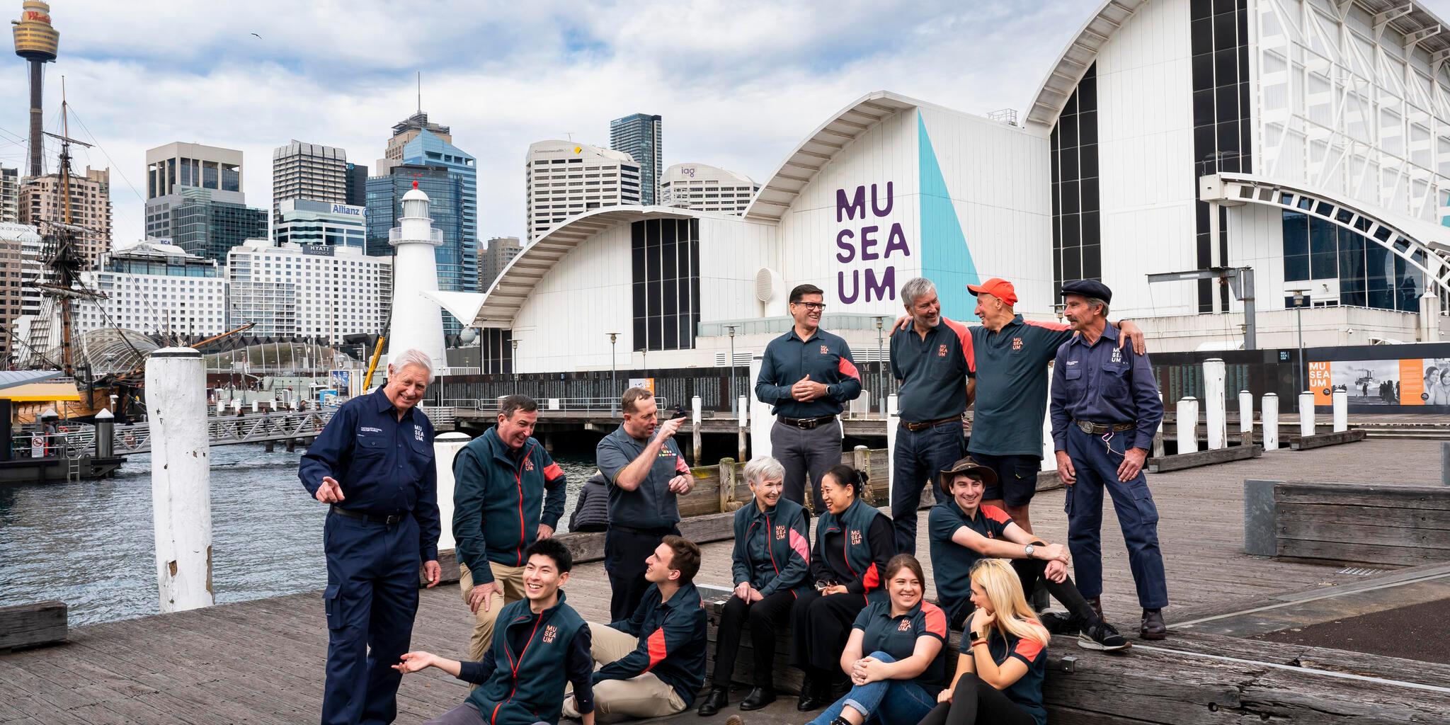 A group of museum volunteers photographed outside Wharf 7 with the museum in the background