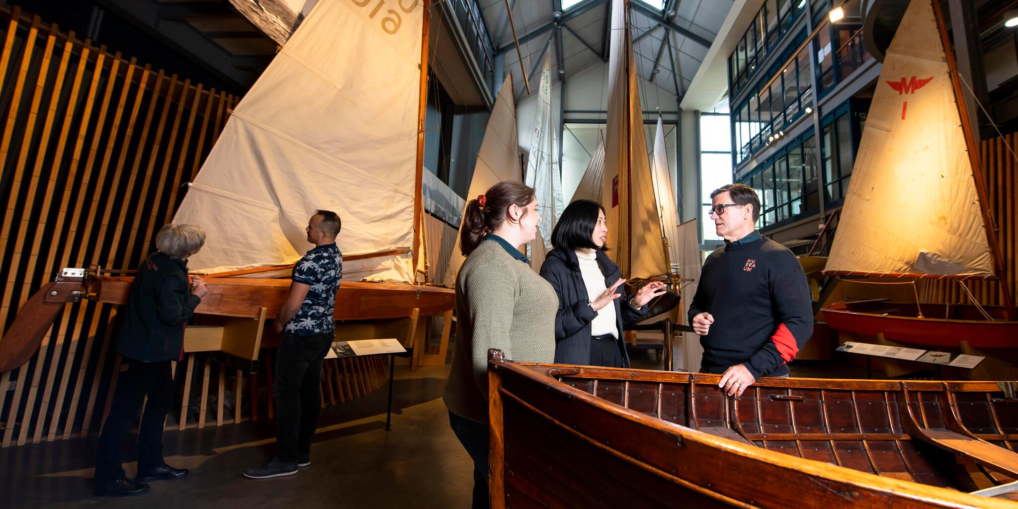 Volunteer giving a guided tour of Wharf 7 foyer heritage vessel display with several other visitors standing around the space..