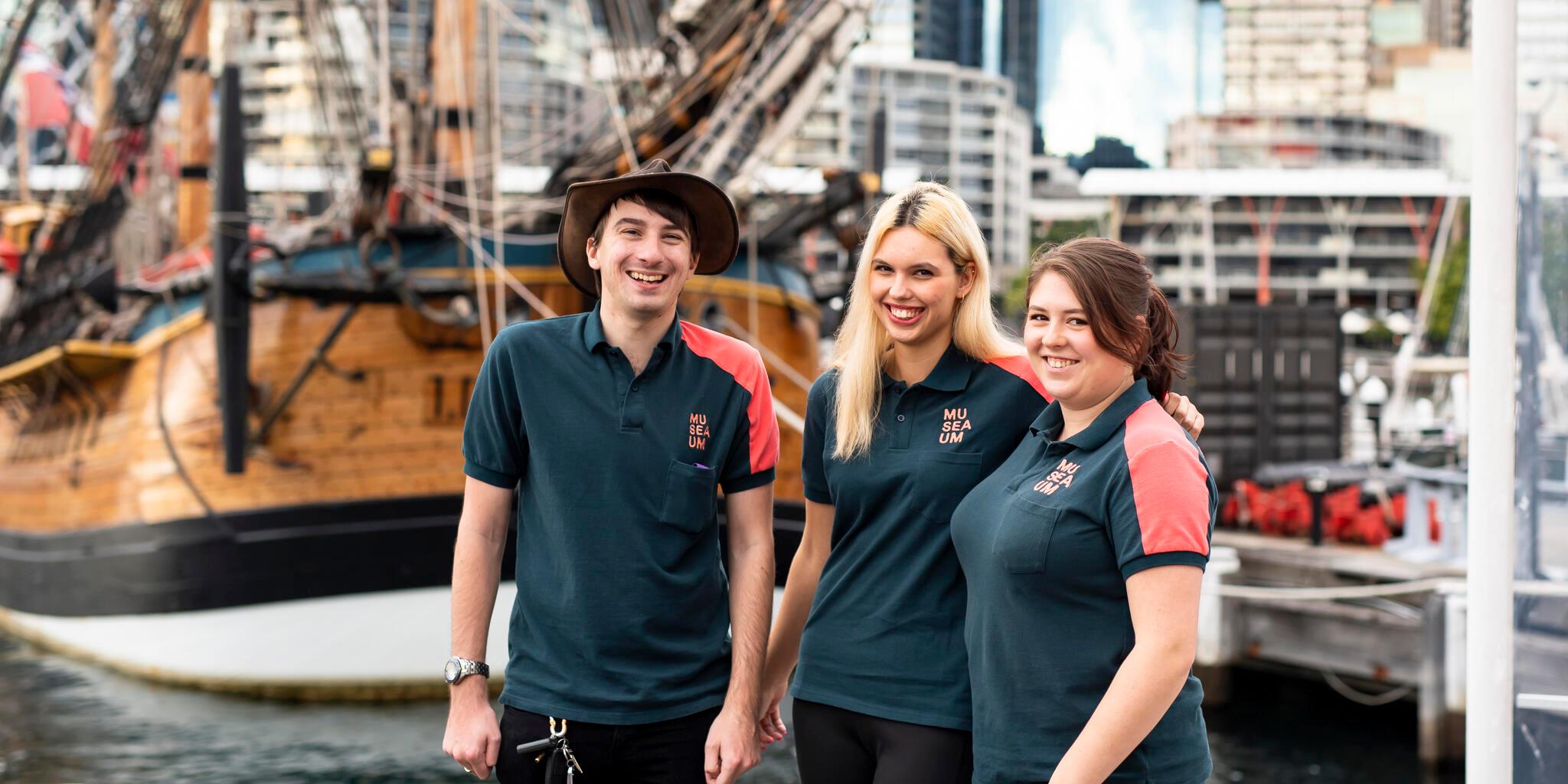 3 volunteers standing on the wharf in front of replica tall ship ENDEAVOUR