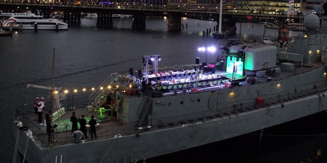 aerial photograph of the rear of navy ship in dim, evening lighting with tables and lighting on the helicopter 