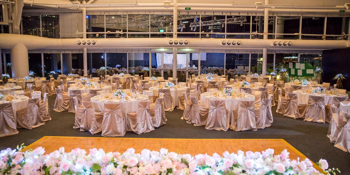 photo of an interior, with chairs and tables decorated in white with flowers for a wedding, with windows in the background.