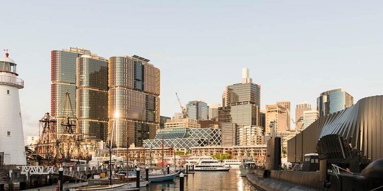 Photo of sydney skyline with a lighthouse and tall ship on the left, and a submarine on the right. 