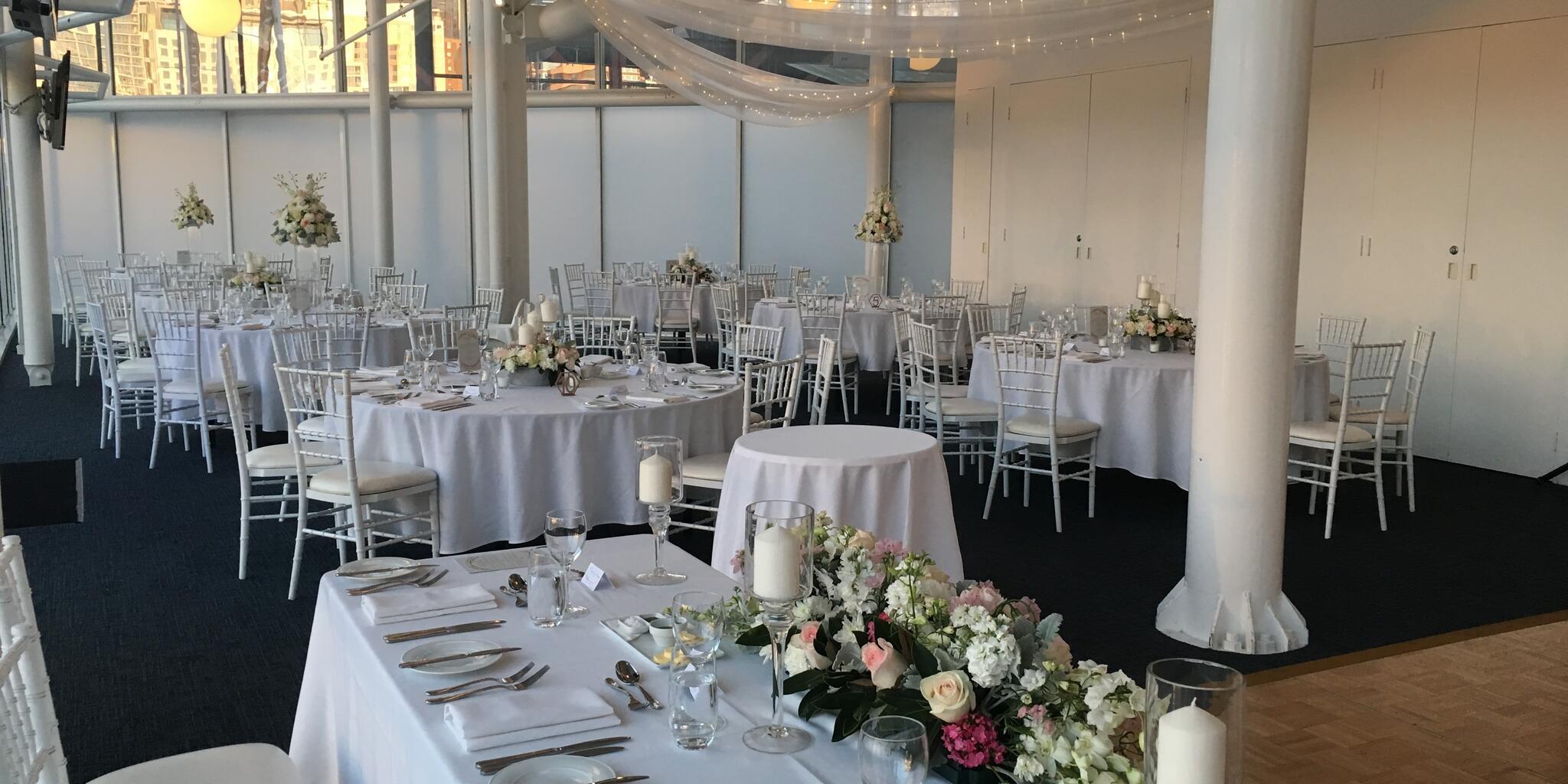 photo of an interior of an event space containing chairs and tables with white tablecloths and place settings.