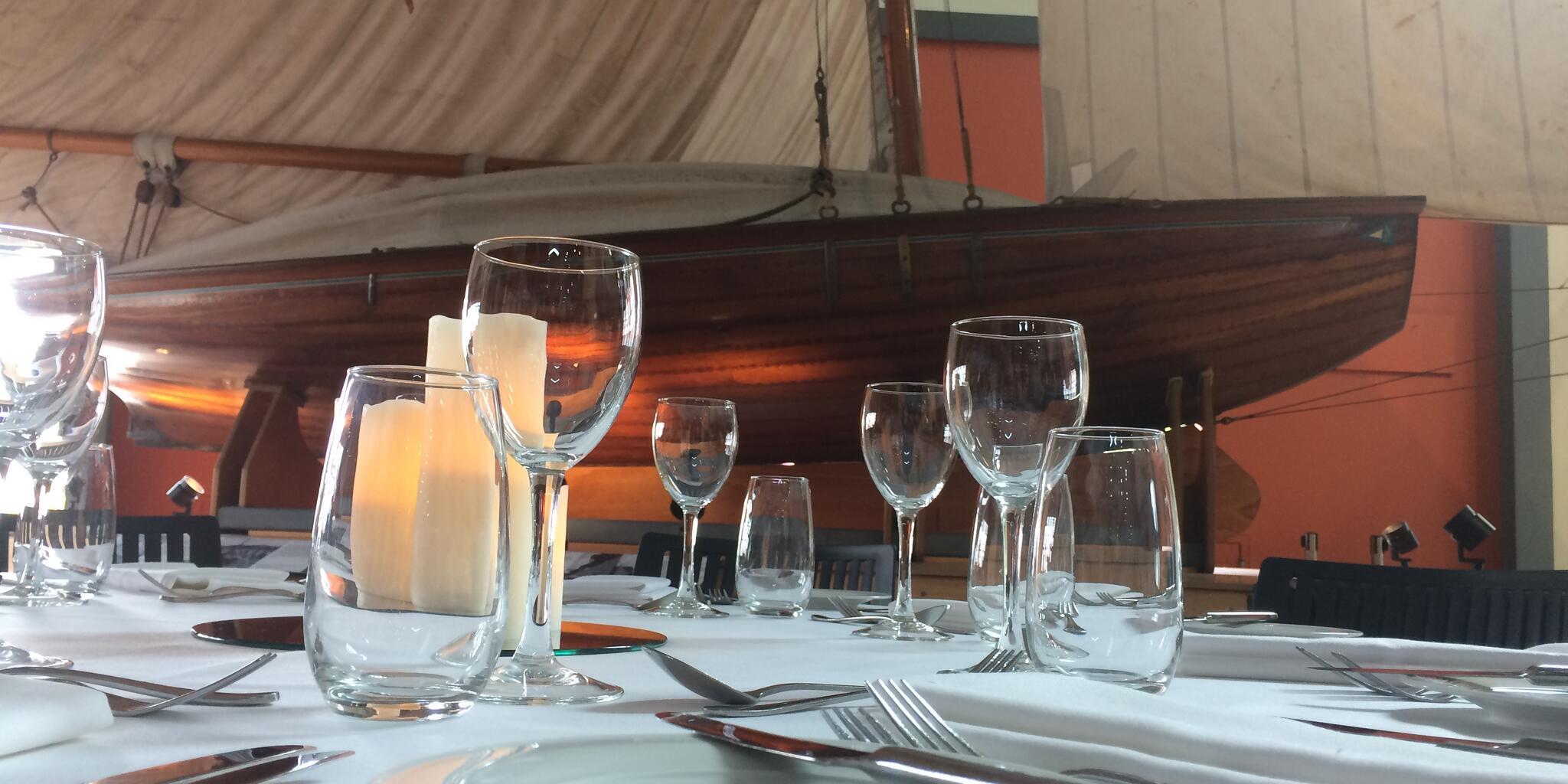 close up photo of a table setting on a white table cloth, with a classic wooden sailing boat in the background.