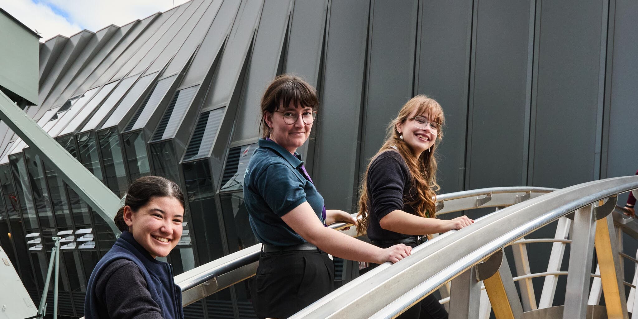 3 female museum educators in dark uniforms on a yellow ship's gangway. 