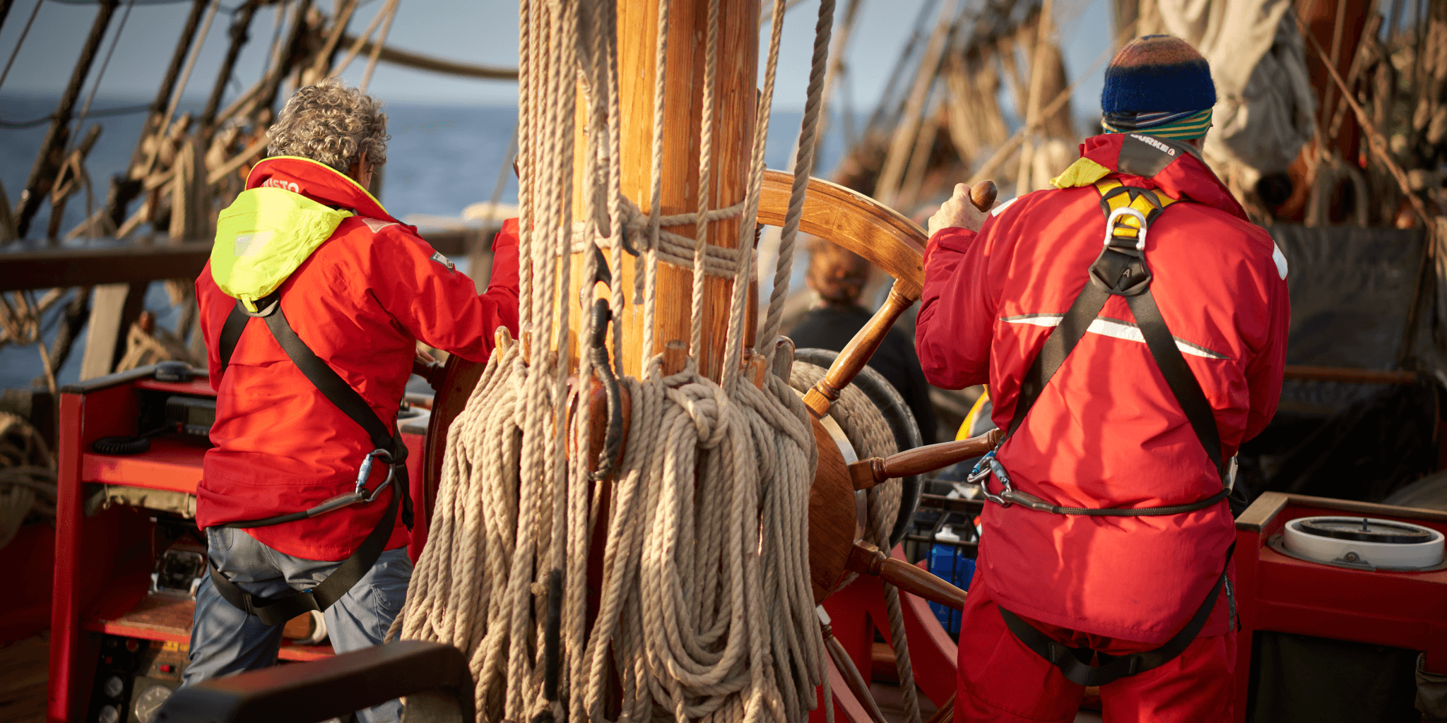 Above deck, voyage crew at the ship's wheel, dressed in wet weather gear. 