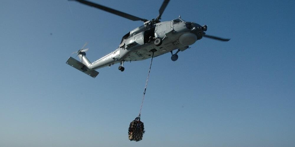 A helicopter flying, a bag of cargo hanging below it. 