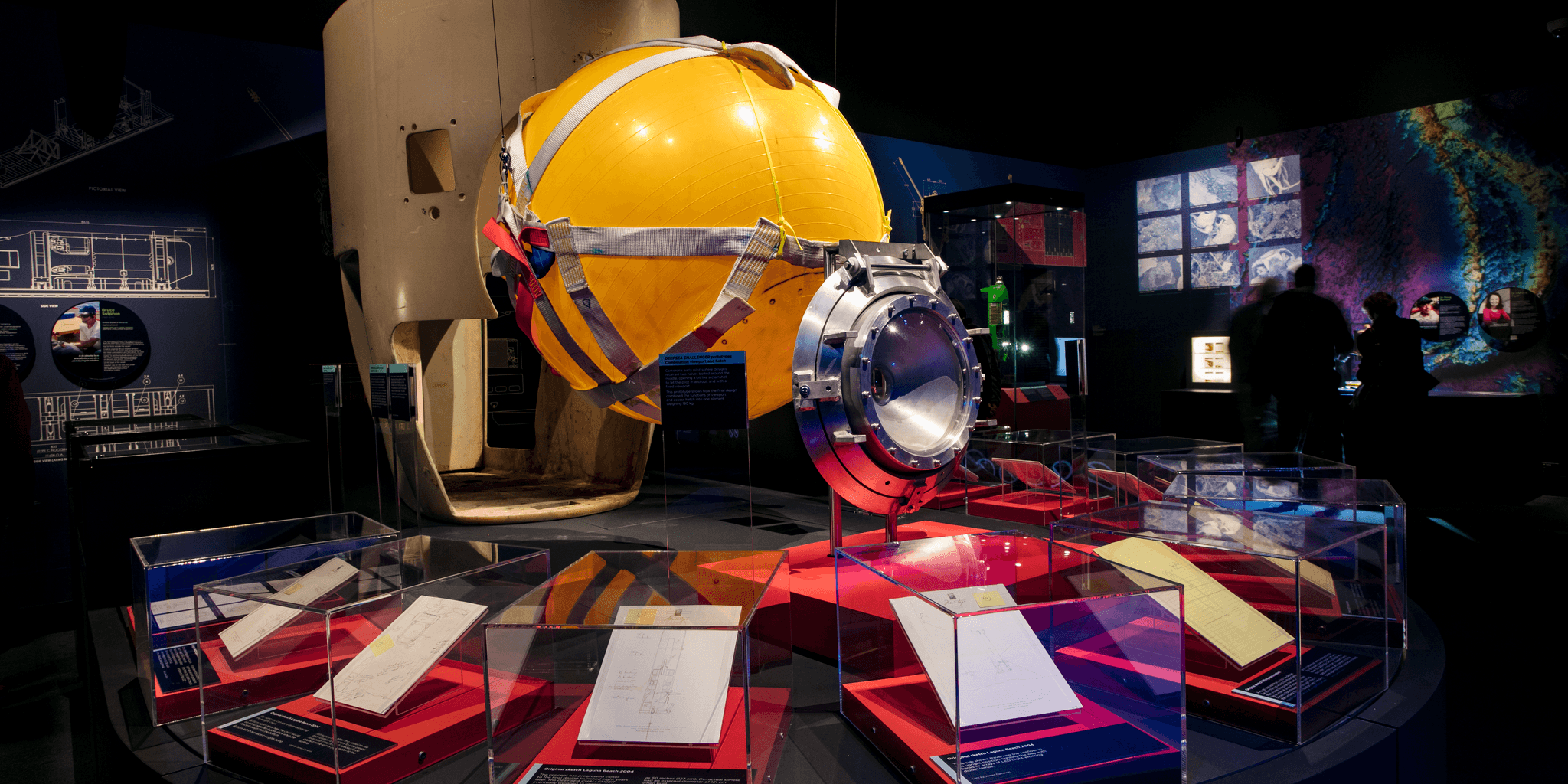 Photo of an exhibition space featuring a large yellow ball surrounded by small display cases.  