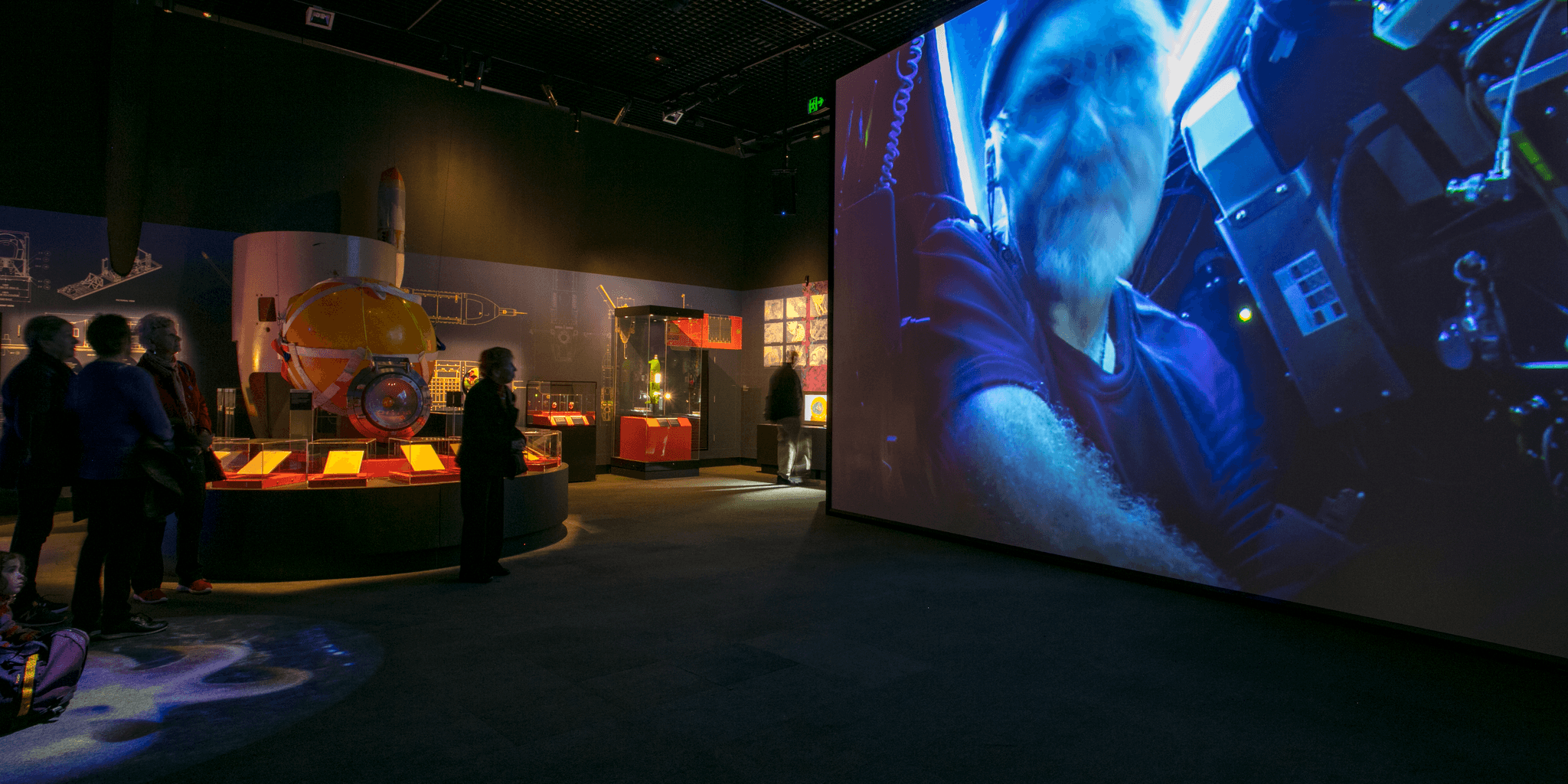 Photo of an exhibition space featuring a large projector screen, with an image of a man, James Cameron.