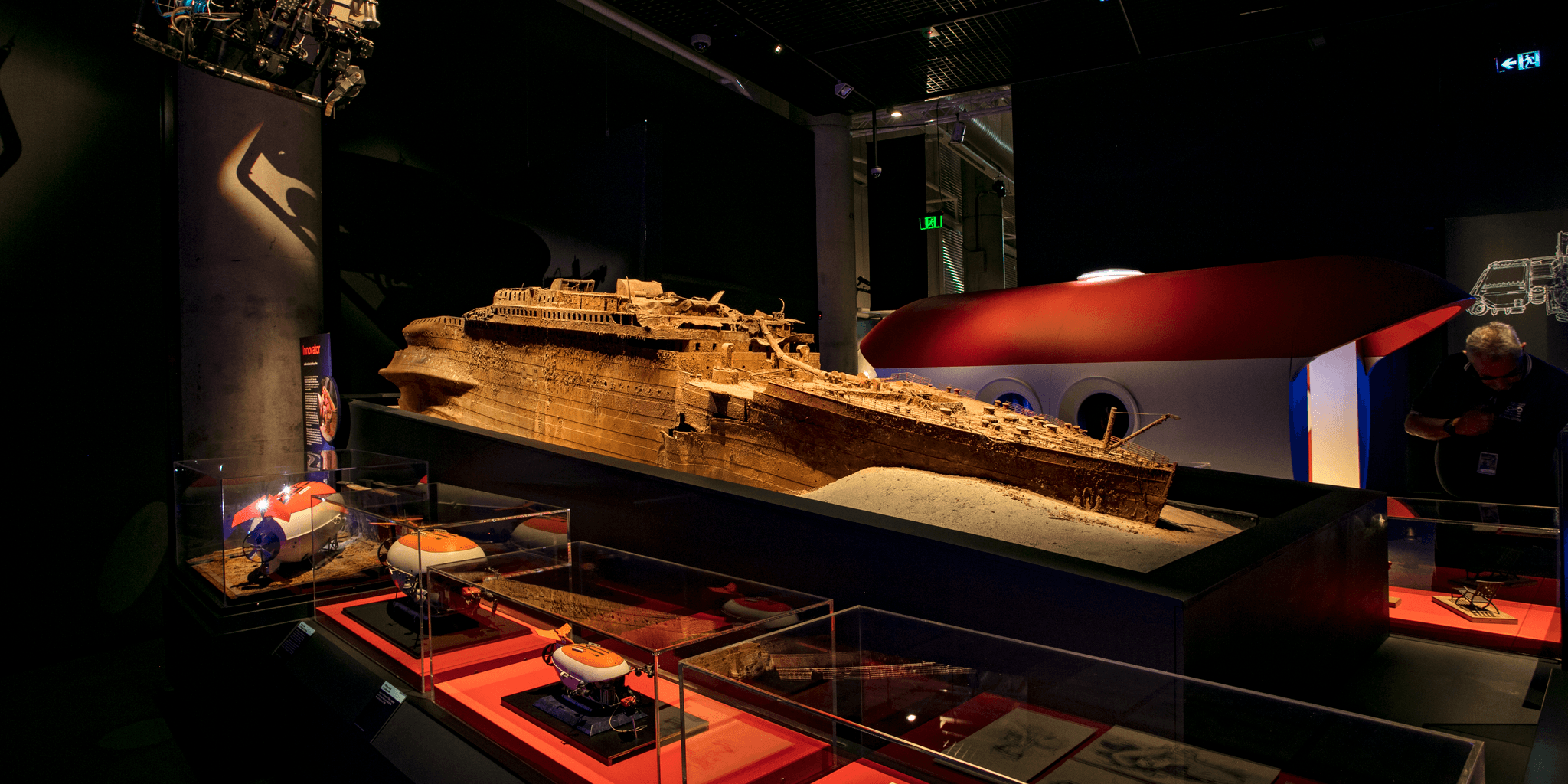 Photo of an exhibition featuring a model of a rusty brown ship (Titanic) and museum display cases. 