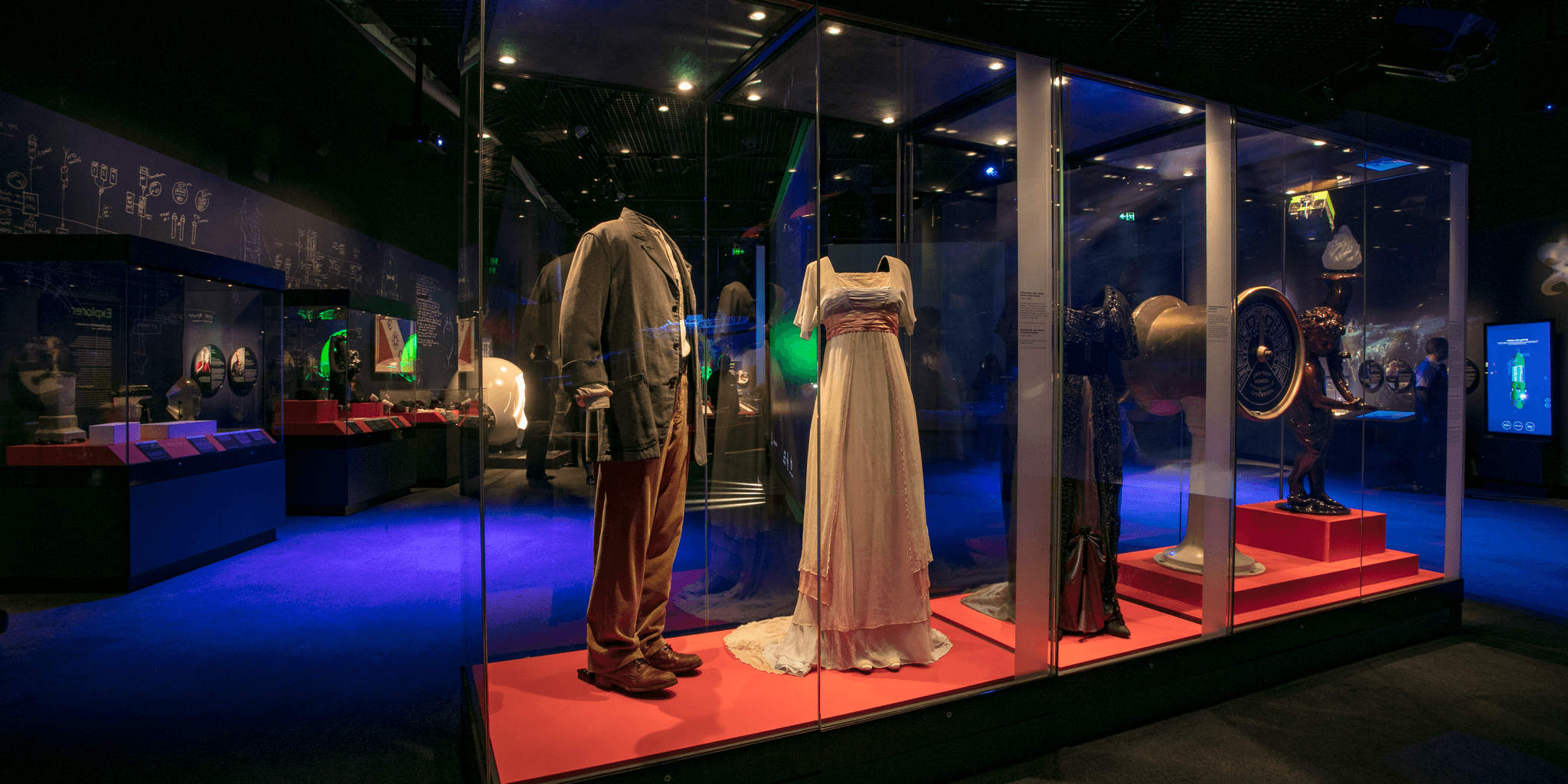 Photo of an exhibition space with a tall display case containing costumes on mannequins.