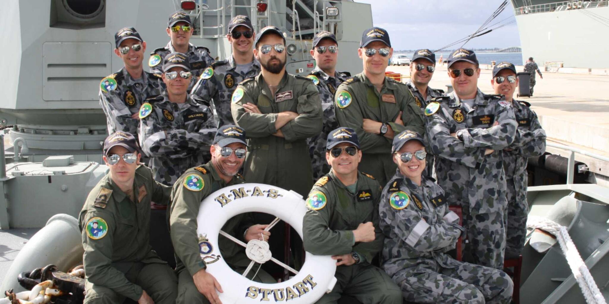 A group of mulirary personel in uniform. The photo is takem outside with everyone wearing hats, sunglasses and gren or camo pattern uniform.