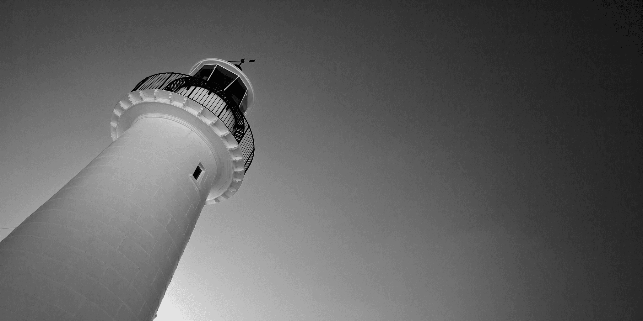 his black and white image shows the museum lighthouse shot from below at an angle lit by the sun from behind.