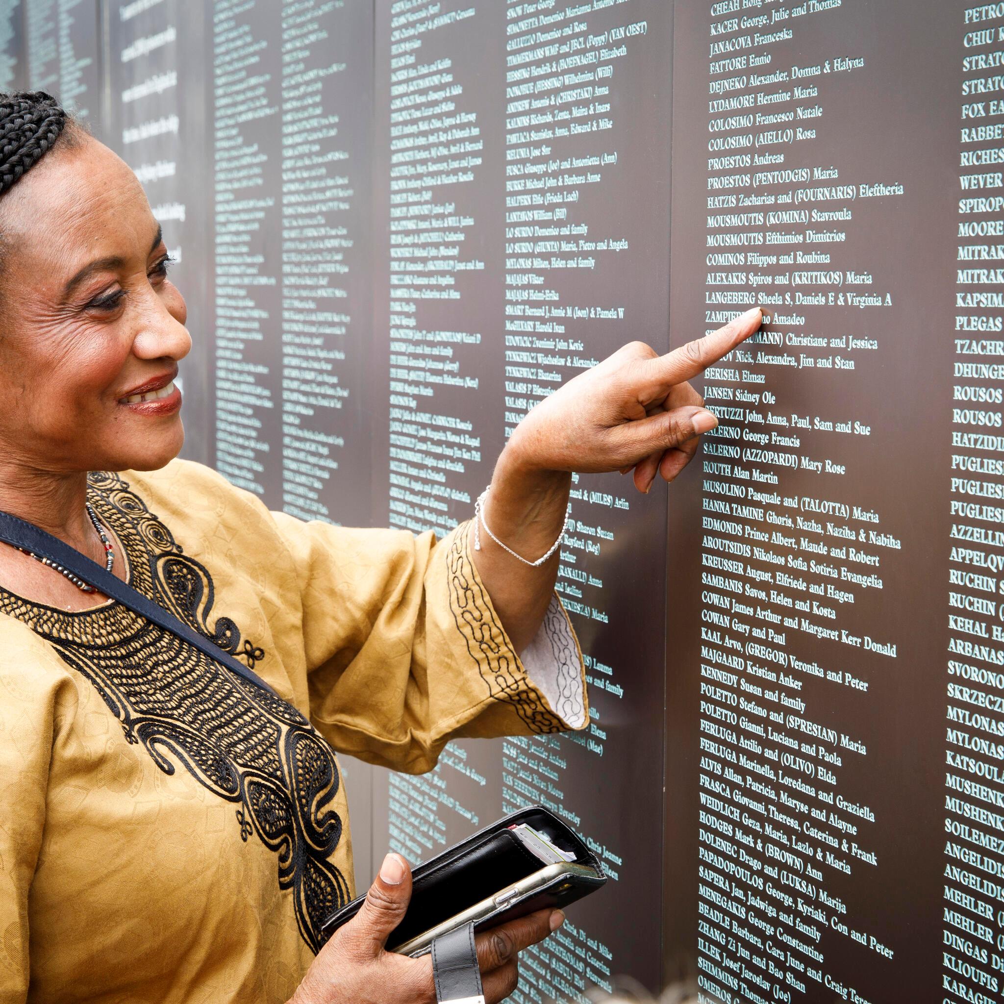 Woman pointing at her family name on the National Monument to Migration