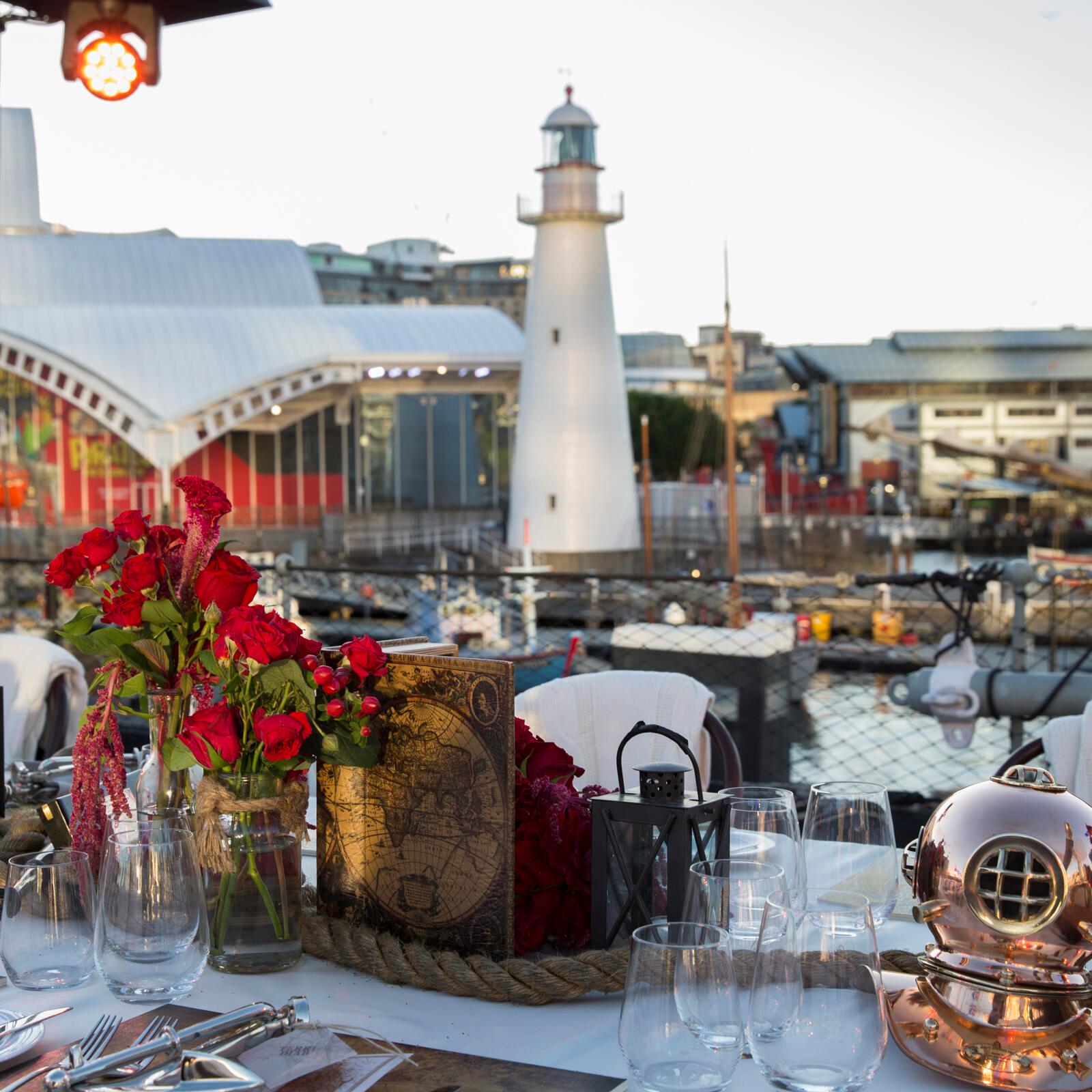 Photo with a table set for an event in the foreground and a white lighthouse in the background.