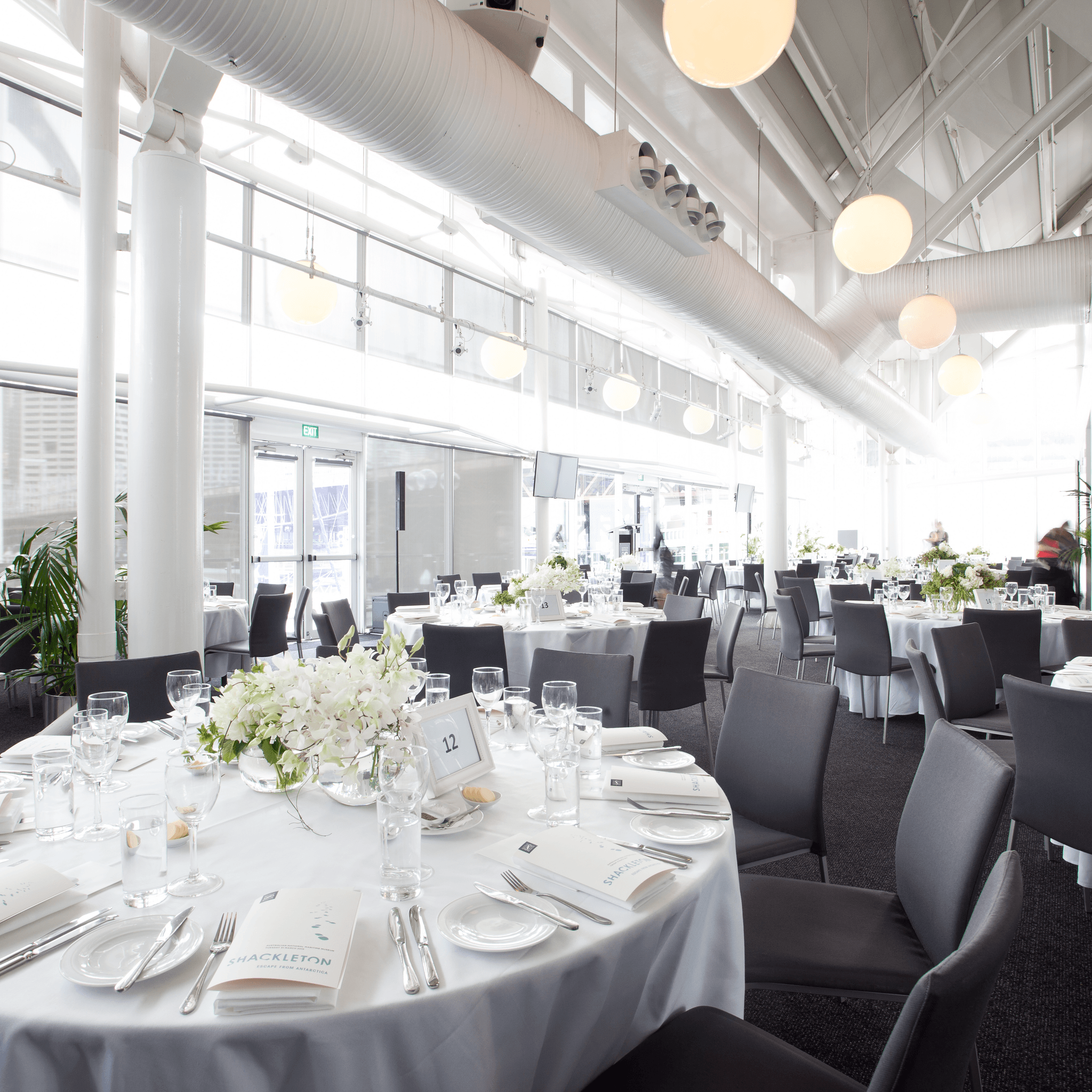 photo of a light filled event space with large round tables set for a formal event. 