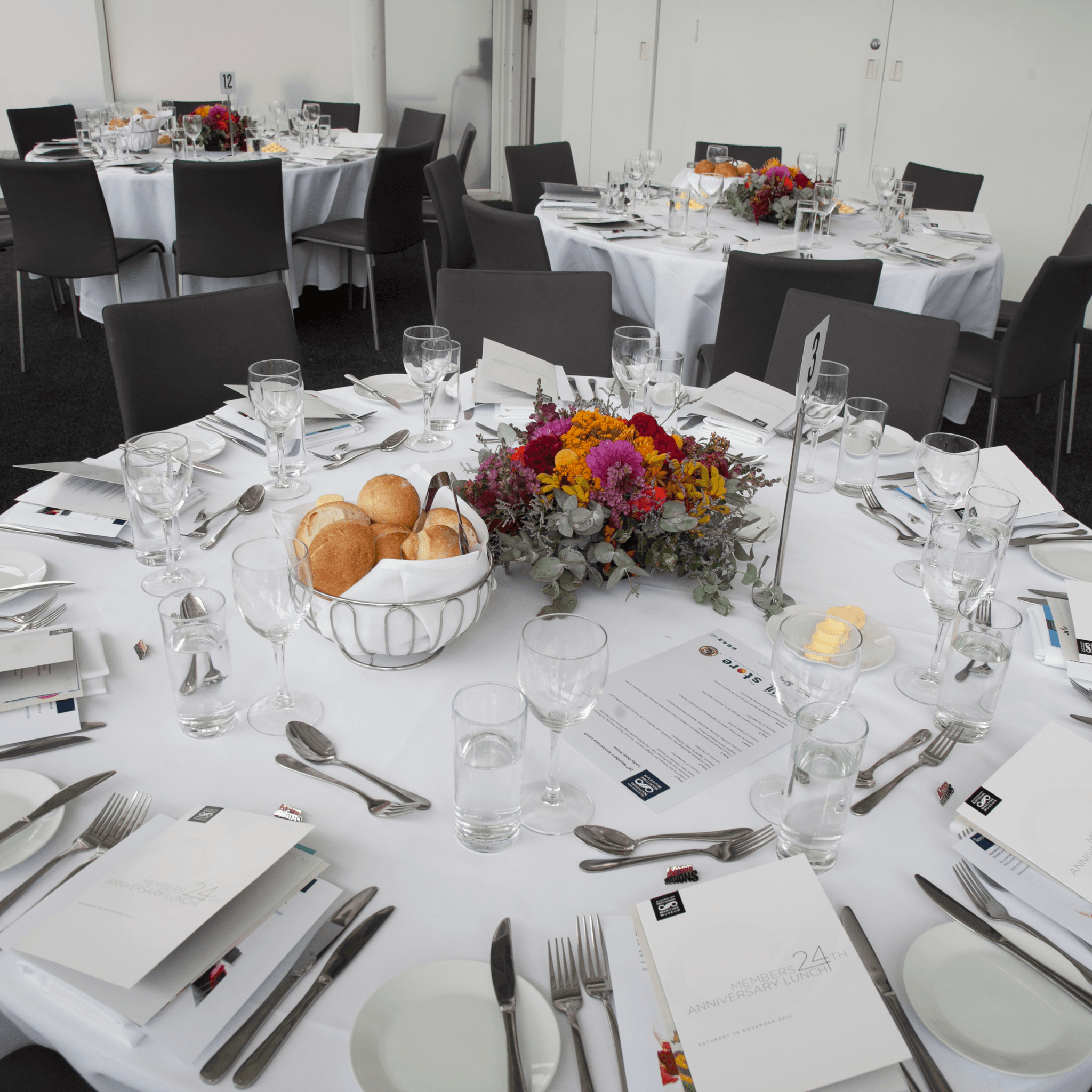 photo of a large round table set with a white tablecloth for a formal event with flowers in the centre. 