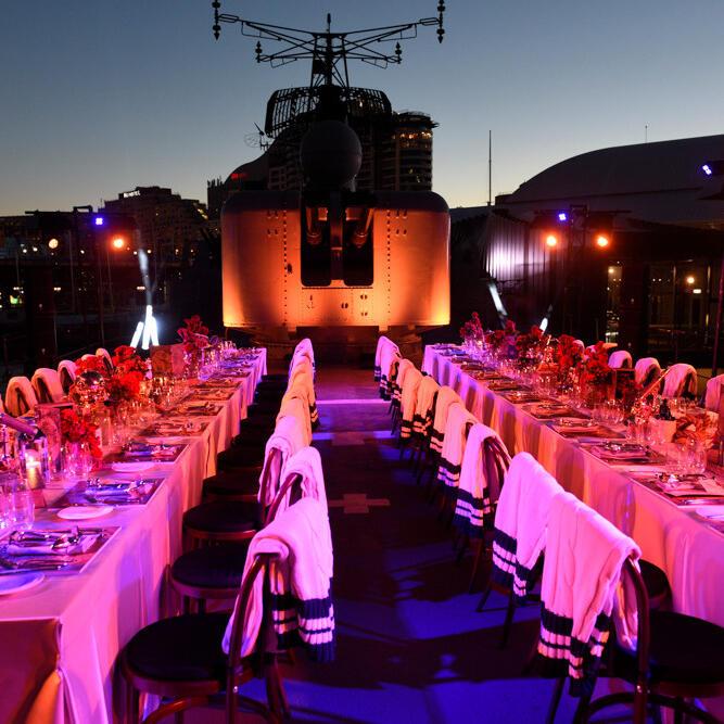 photo of the deck of a navy warship at dusk, with long tables set up for a formal event and intense pink lighting