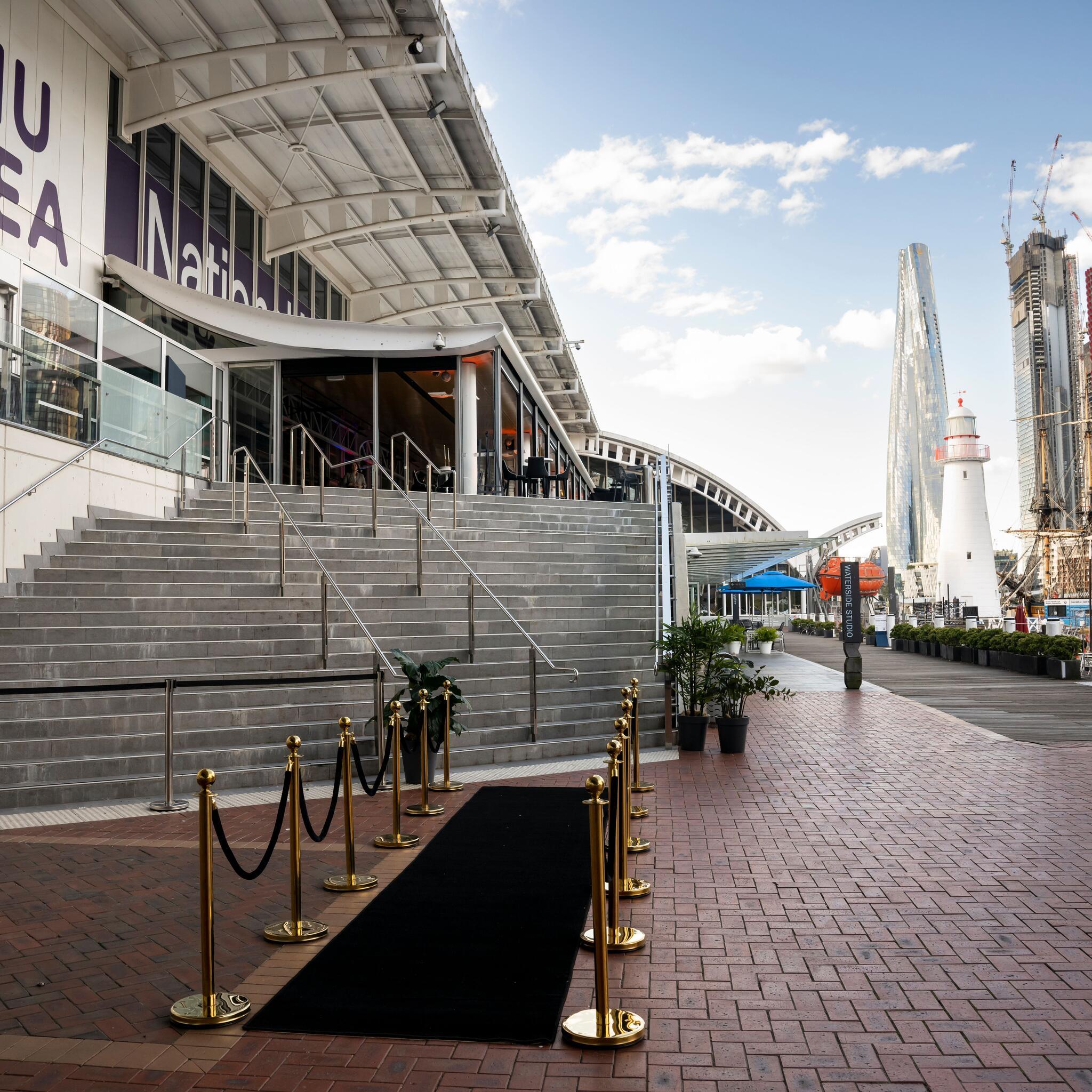 photograph on a sunny day with a blue sky with a building and wide staircase on the left side and waterside walkway on the right