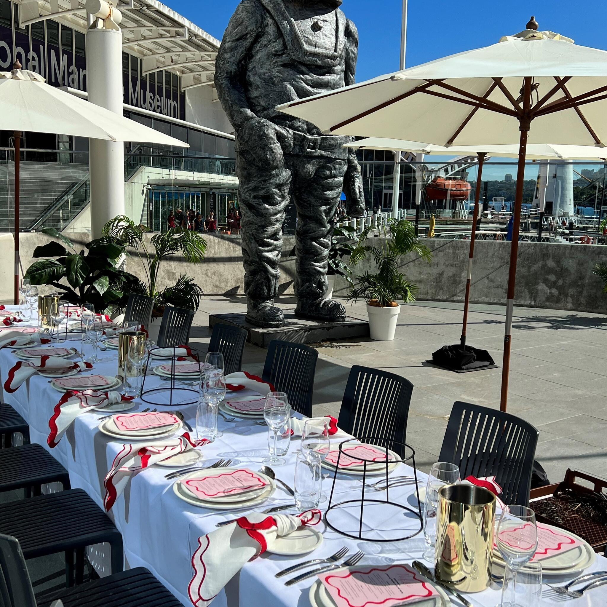 photo of a table and place setting on an outside balcony, with an umbrella and a statue in the background