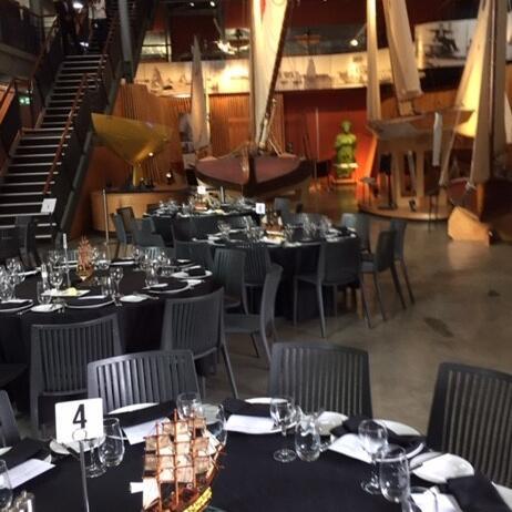 photo of event tables with set and decorated in front of wooden sailing boats. 