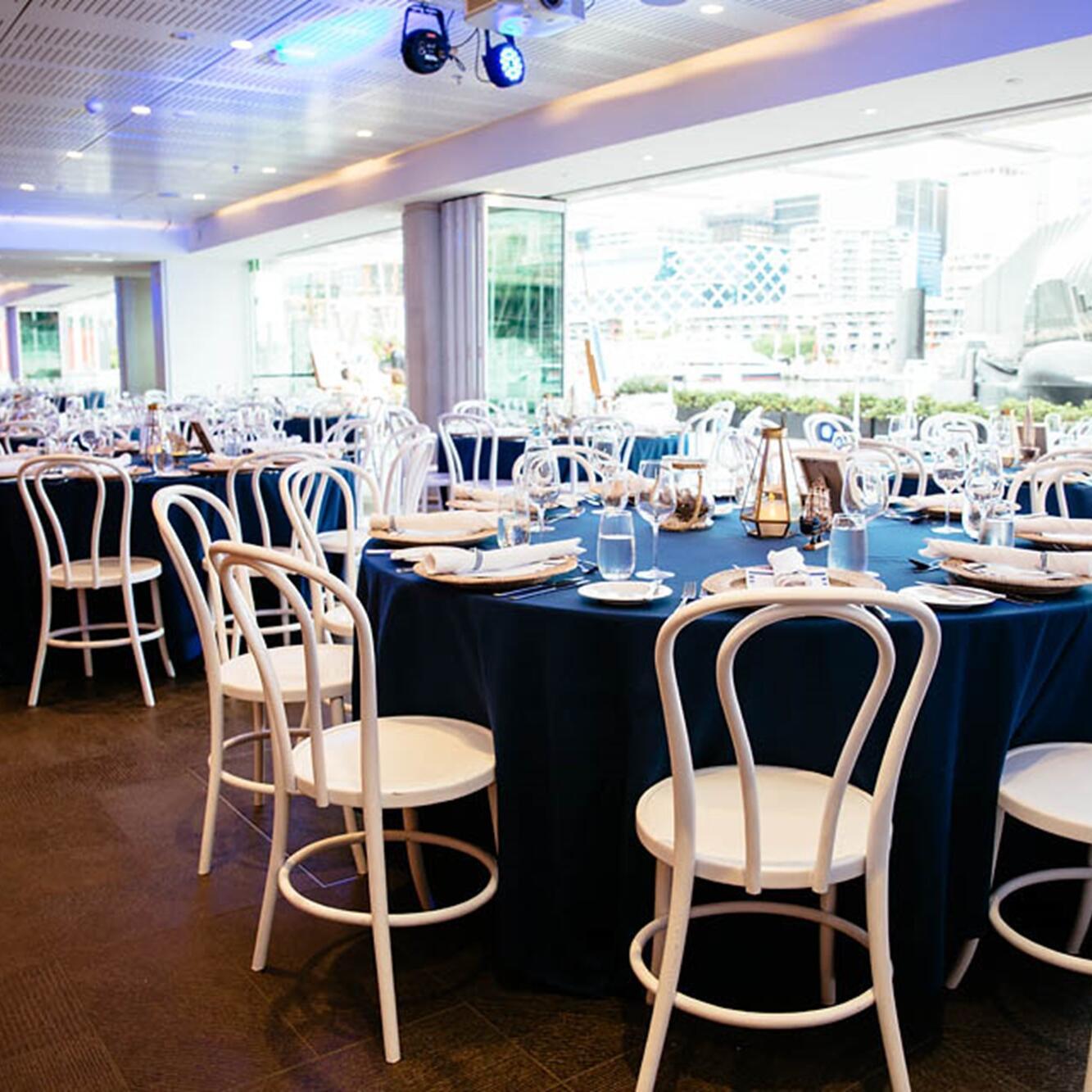 photo of event space with white chairs and large round tables with dark table cloths and place settings. 