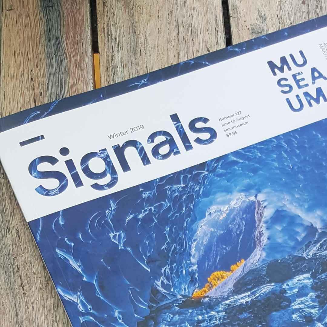 Cover of signals magazine, with an images of a blue wave. the magazine is sitting on a wooden table.