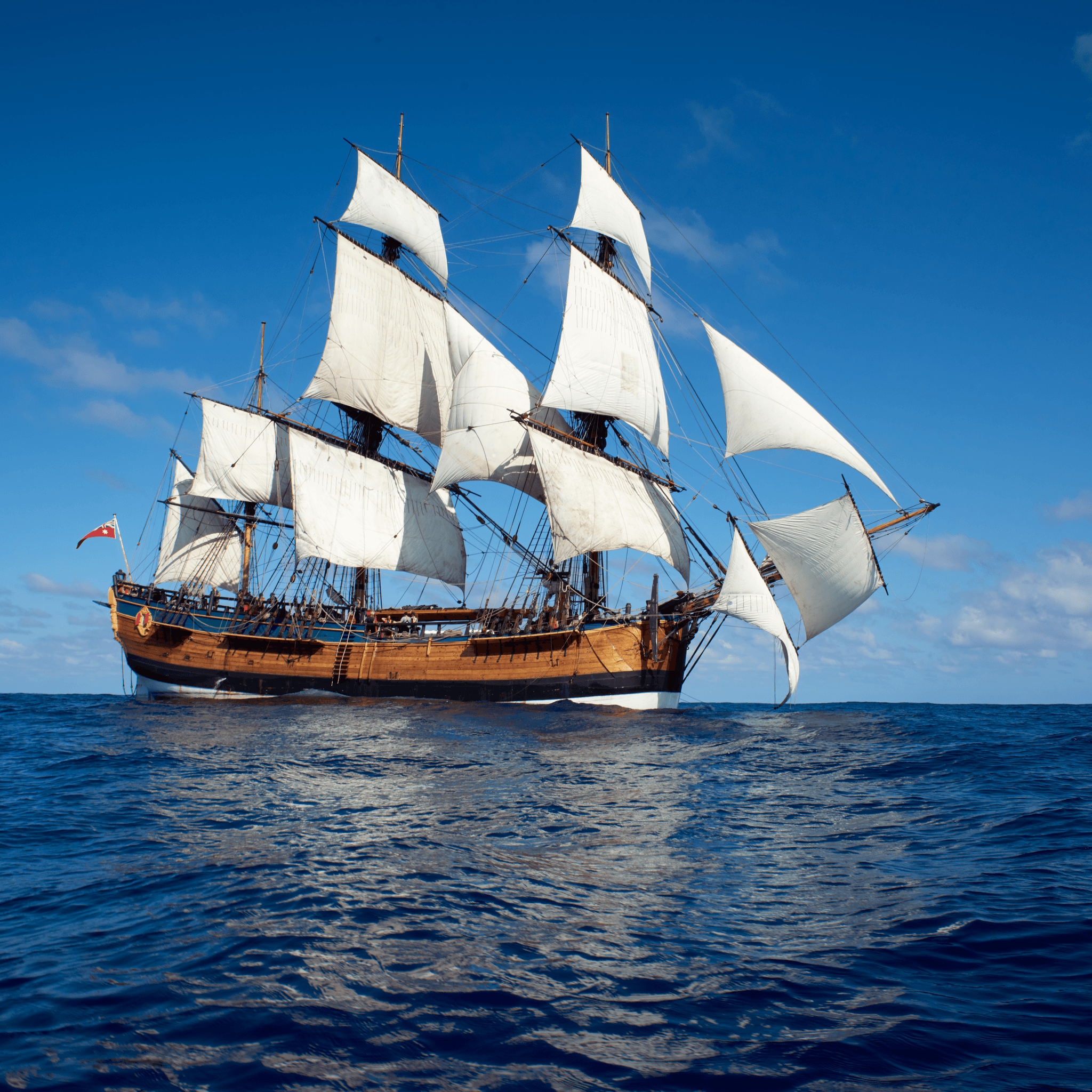 Photo of a tall ship with white sails on a bllue ocean with a blue sky. 