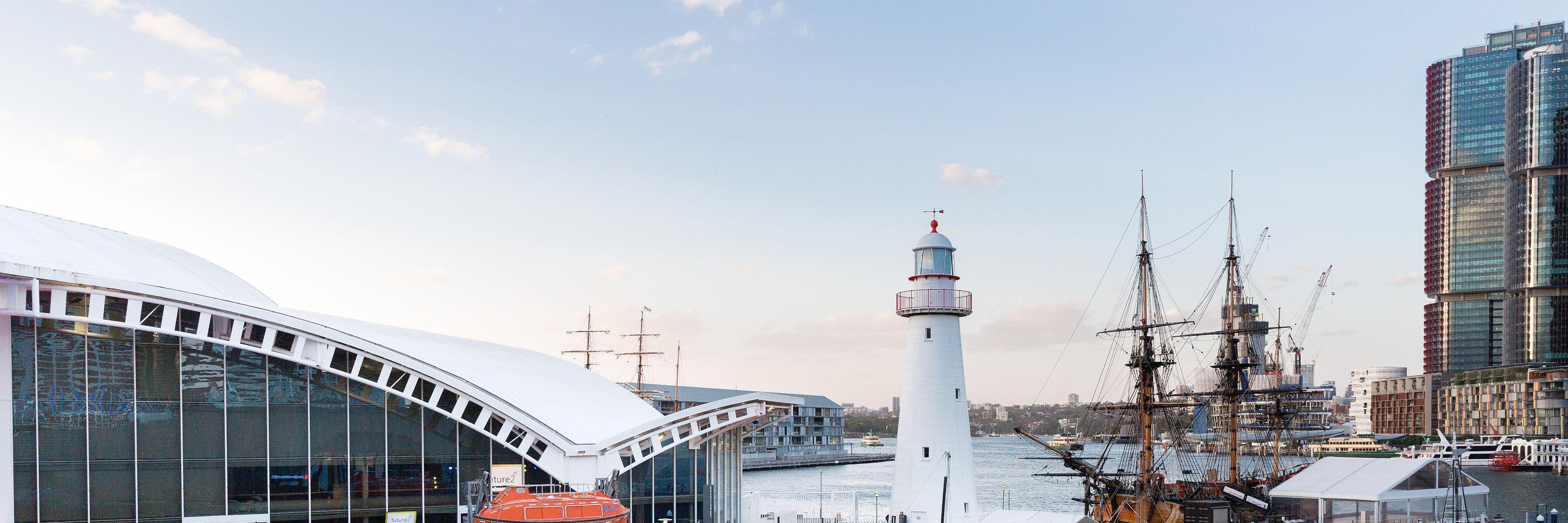 The museum precinct filled with crowds during a corporate event. museum building on the left, with lighthouse and tall ship on the right.