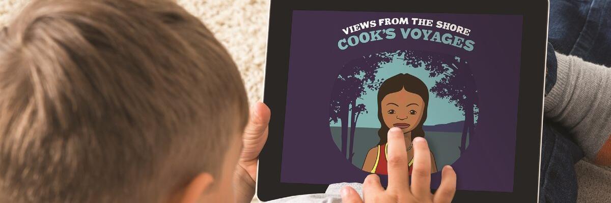 A boy holds an ipad showing a purple screen saying "Cook's Voyages" and an image of an aborigional girl. 