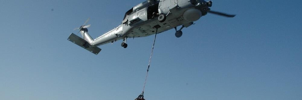 A helicopter flying, a bag of cargo hanging below it. 