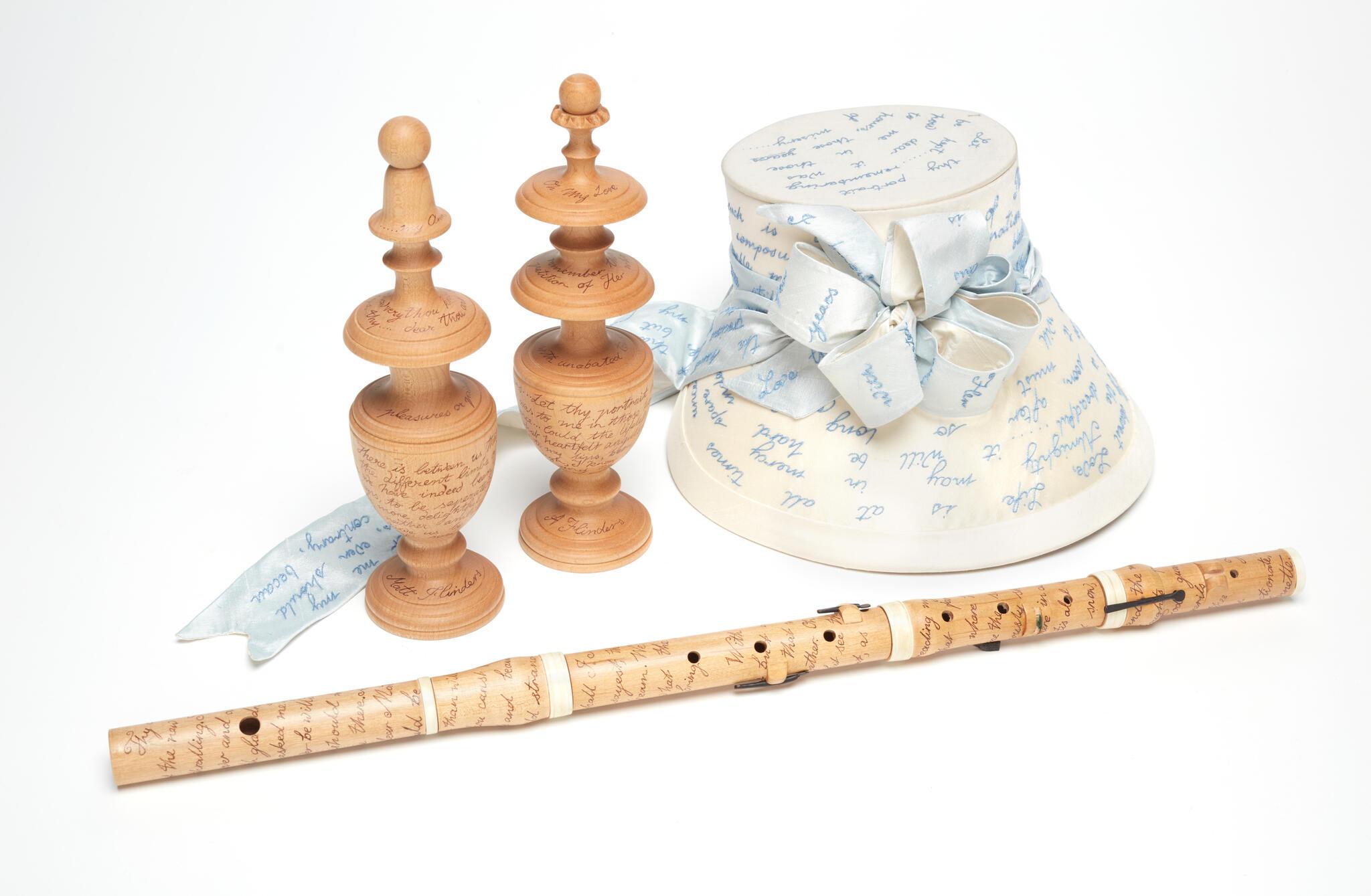 collection of sculptures including a white bonnet, 2 wooden chess pieces and a wooden flute. 