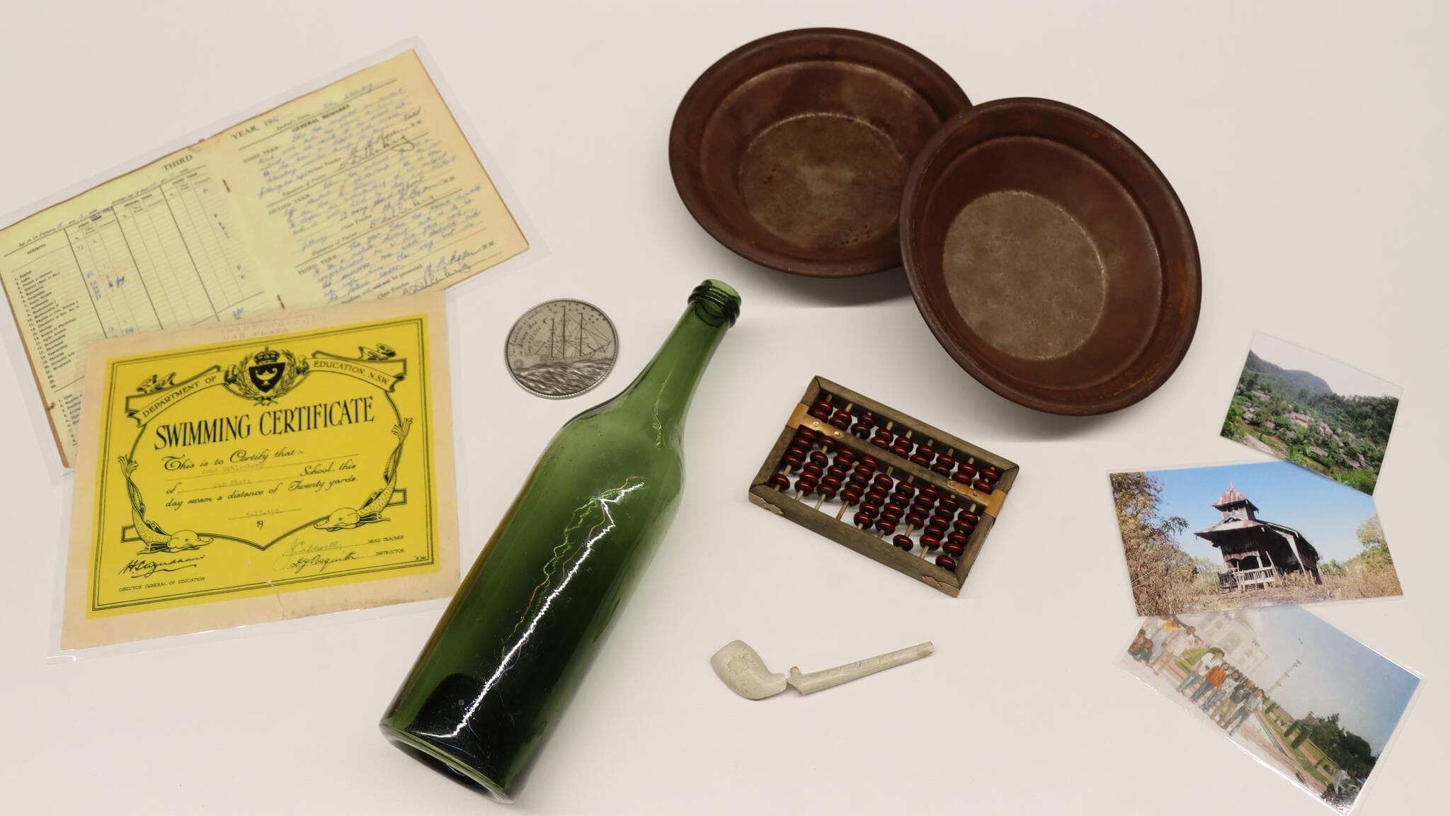 Collection of objects used in education program, including a green glass bottle, a broken clay pipe, metal gold pans, photographs and laminated certificates.  