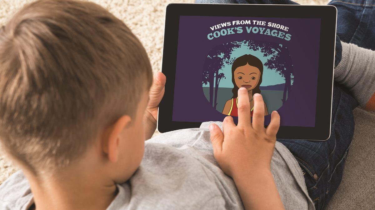 A boy holds an ipad showing a purple screen saying "Cook's Voyages" and an image of an aborigional girl. 