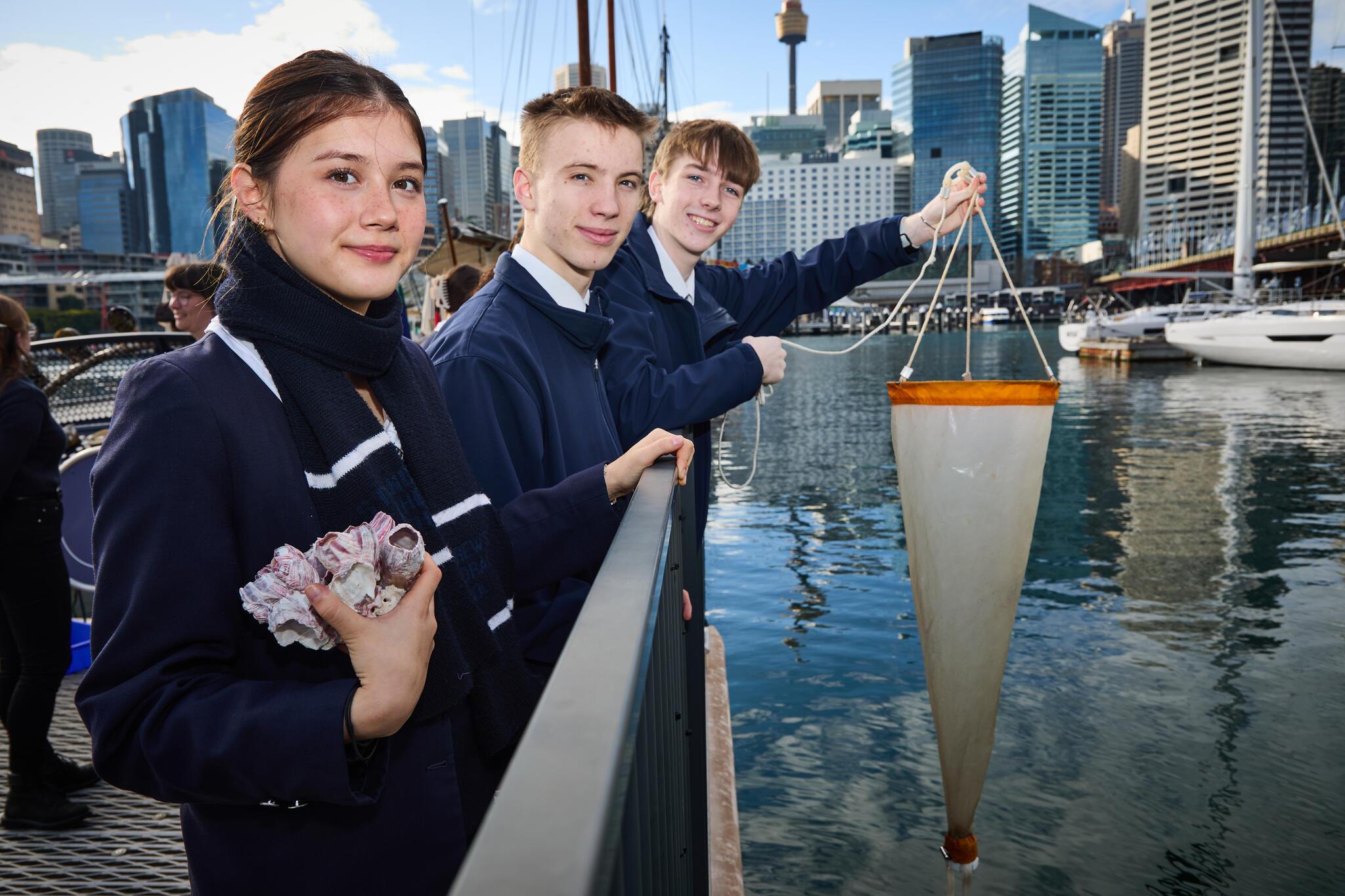 3 high school students in navy uniform on the museum wharf with sydney in the background.